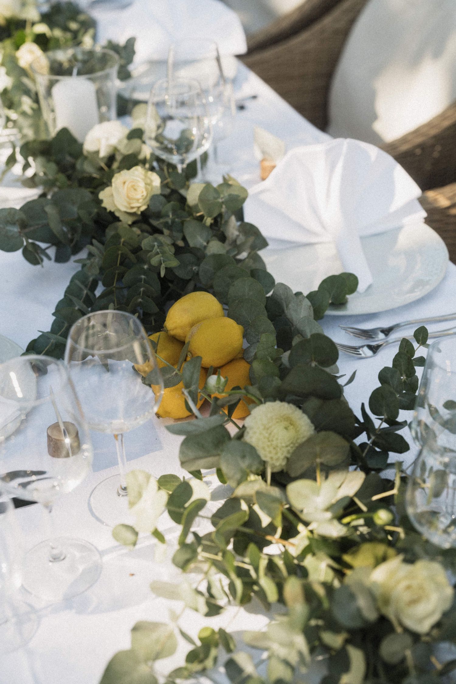 Wedding tablescape featuring white roses, eucalyptus garland, fresh lemons, and crystal glassware.