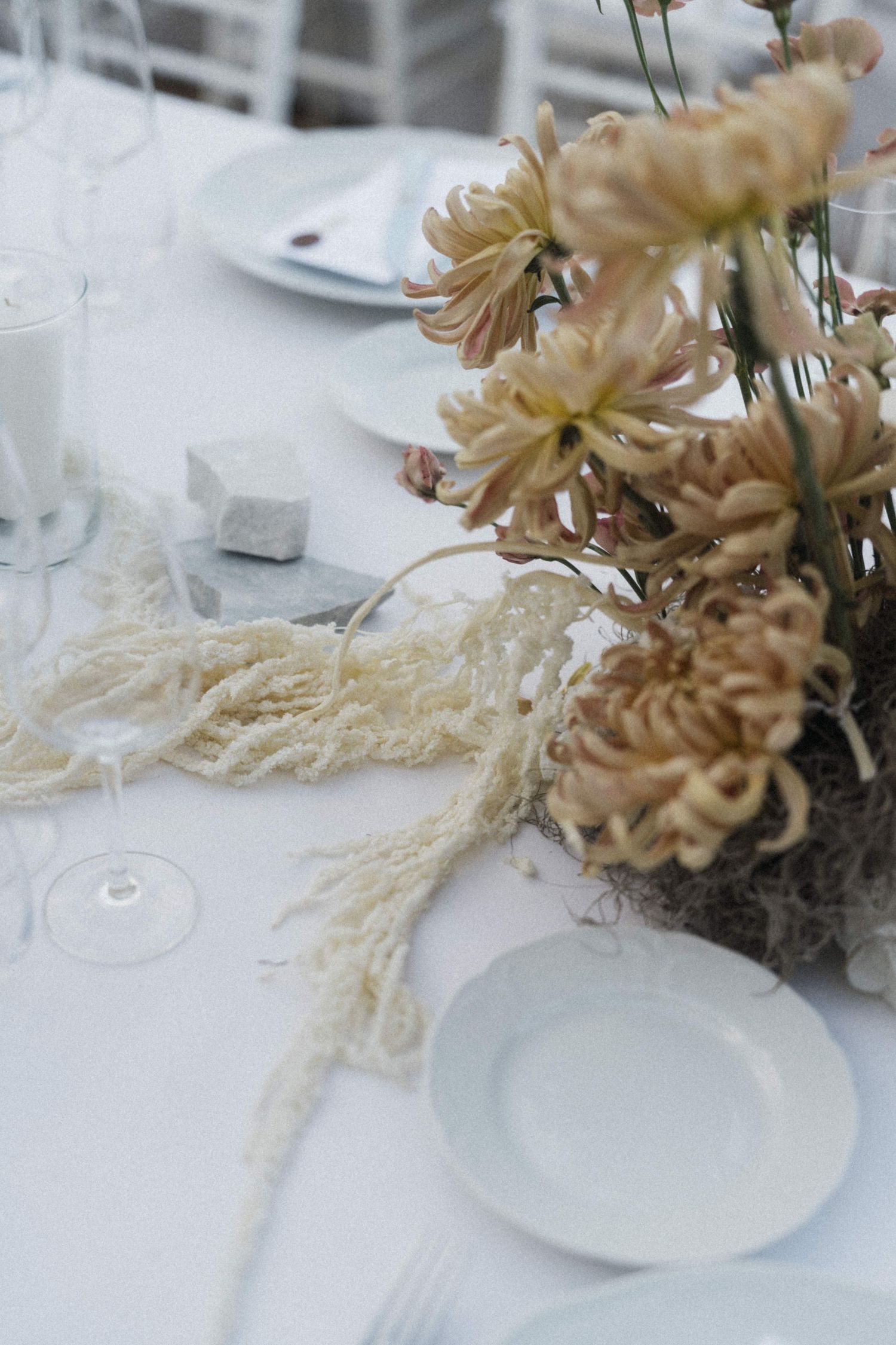 Close-up of wedding table with dried chrysanthemum centerpiece, macrame detail, white plates, and crystal glassware.