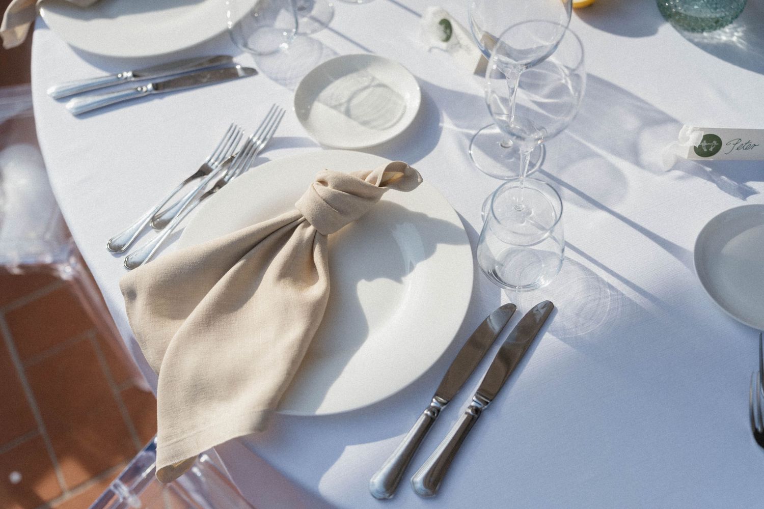 Elegant white table setting with folded linen napkin, silverware, crystal glasses, and white plates for a formal dinner.