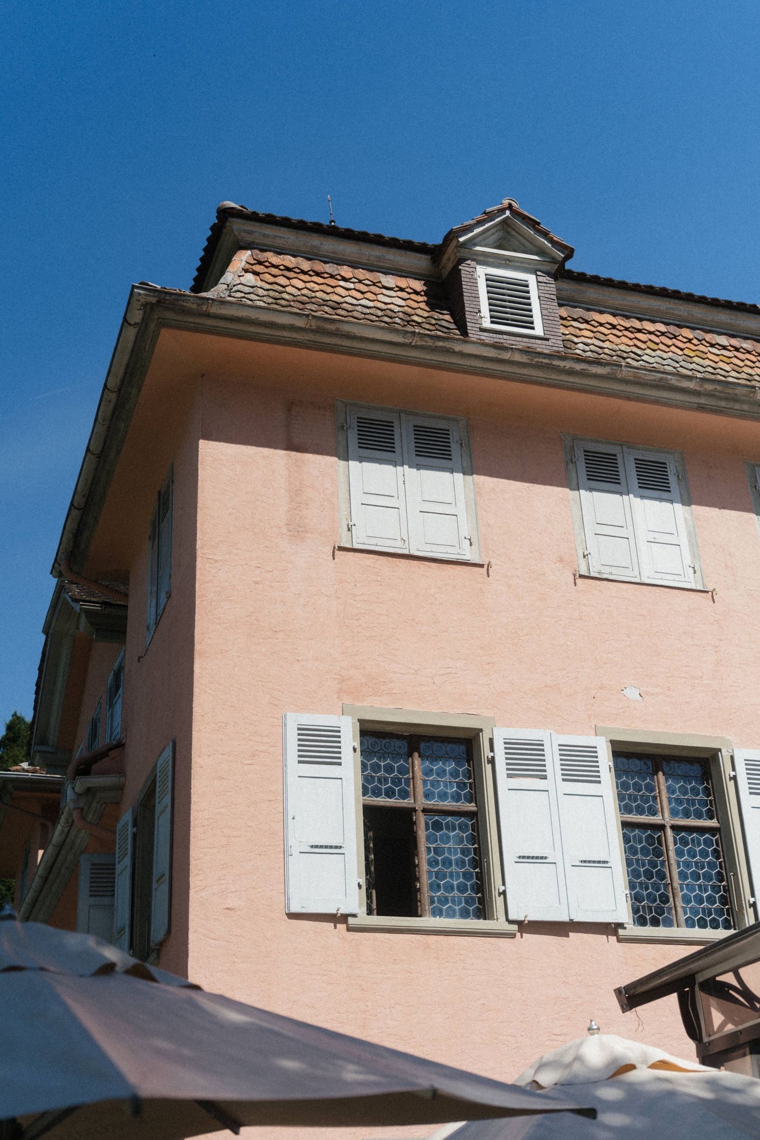 Pink stucco European villa with white shuttered windows against clear blue sky.