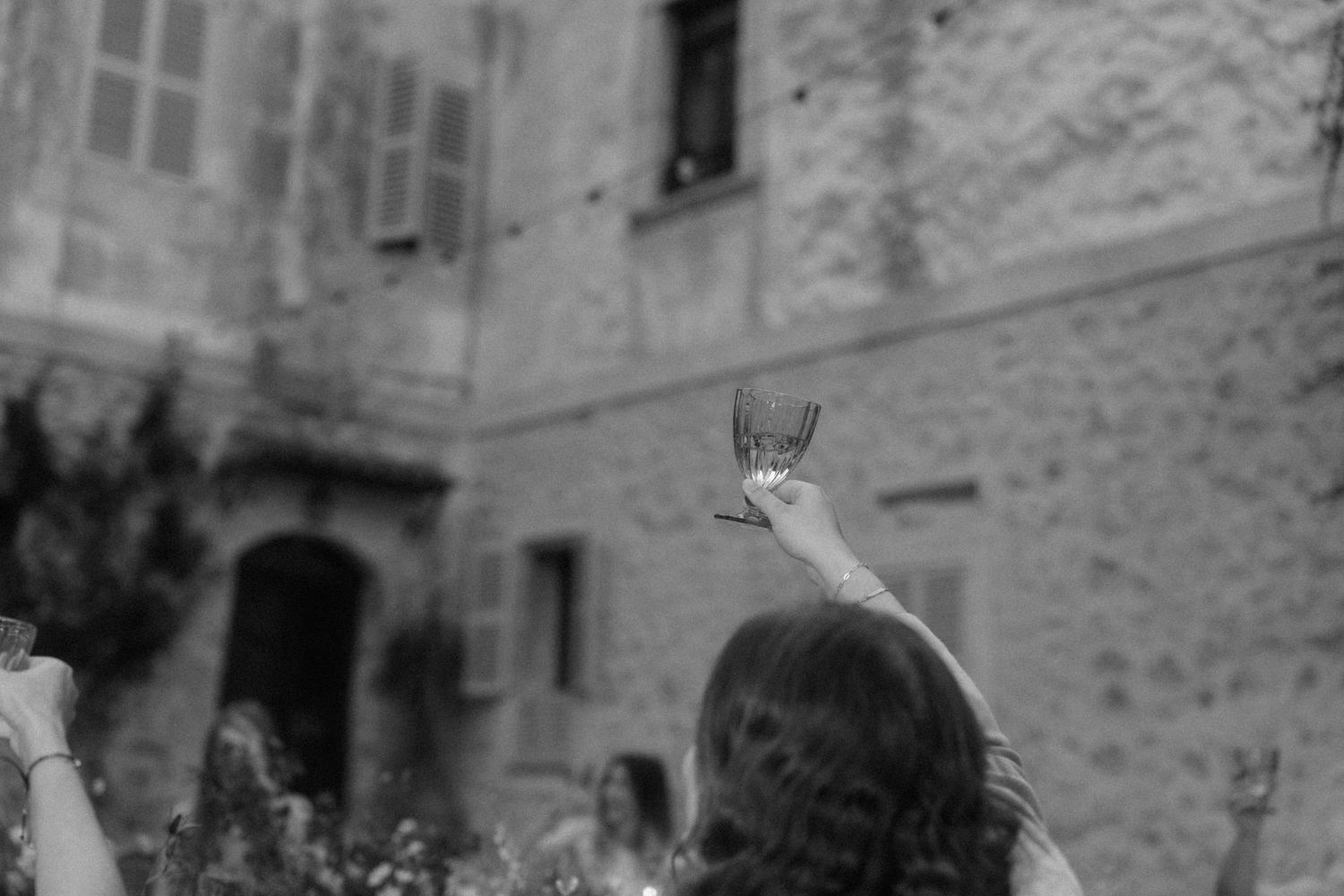 Black and white photo of a woman raising a champagne glass at an outdoor wedding celebration.