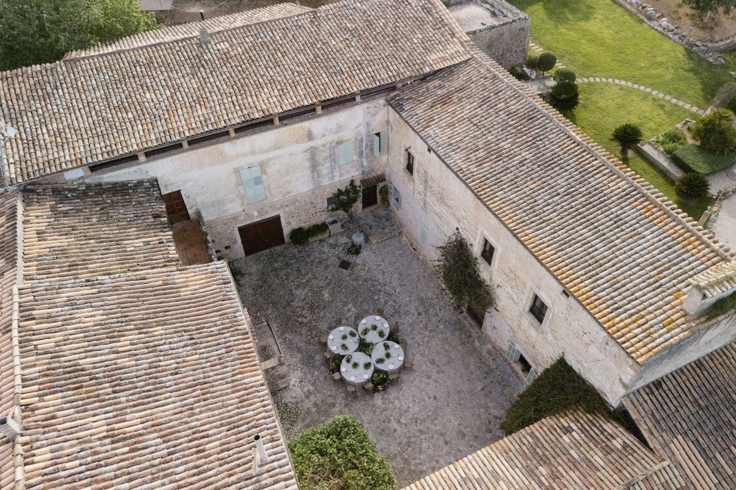 Aerial view of a historic stone courtyard with terracotta roof tiles and an elegant round dining table setup.