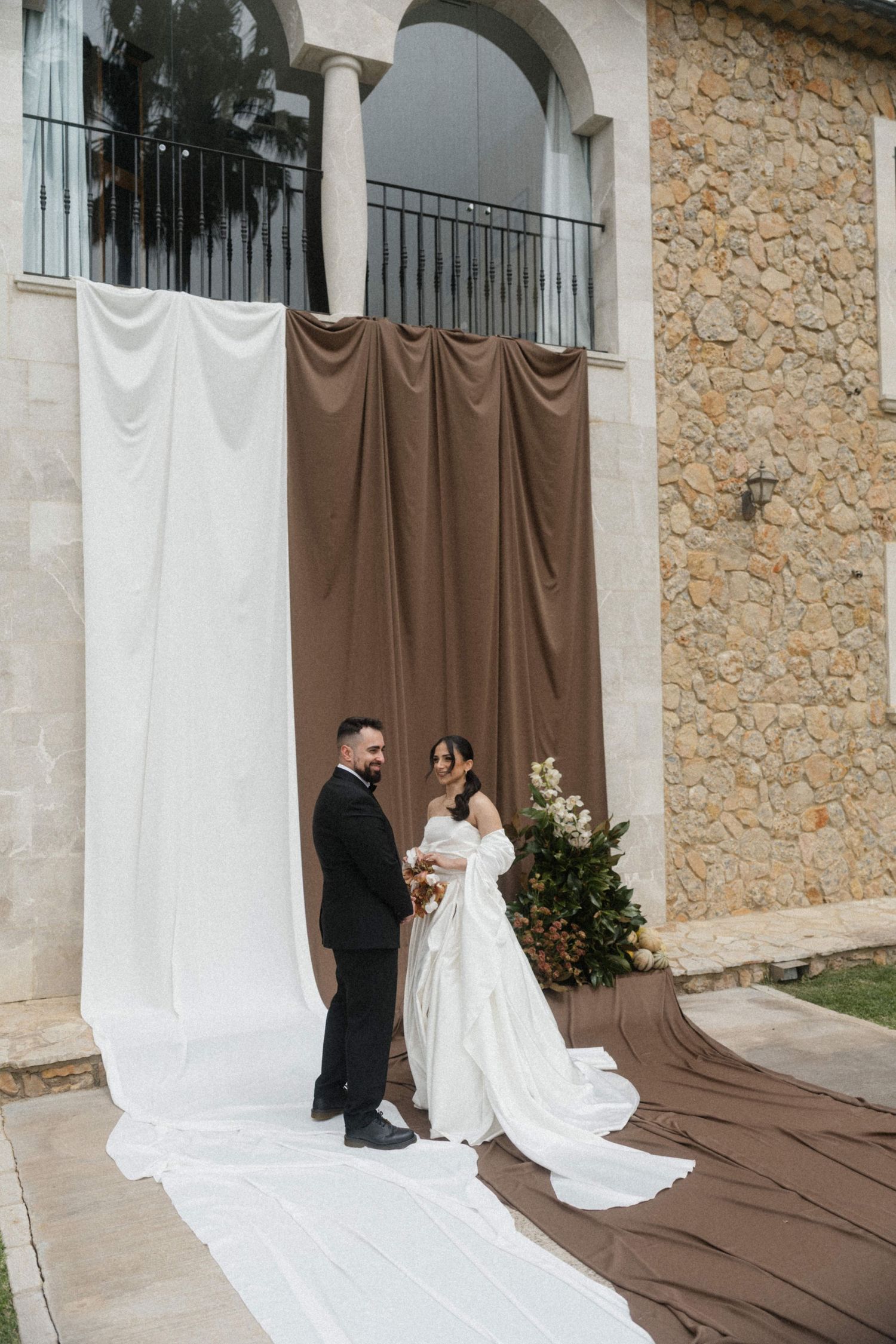 Bride and groom standing before elegant white and brown draped fabric backdrop at outdoor wedding ceremony.
