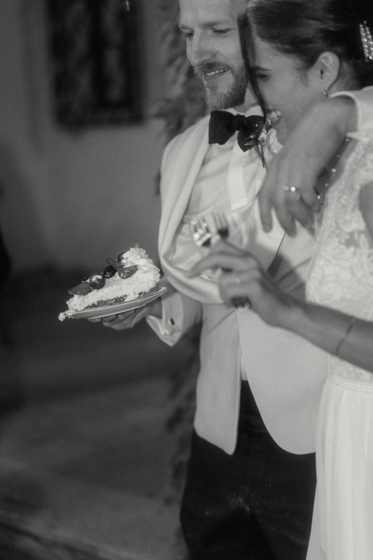 Black and white photo of smiling bride and groom cutting their wedding cake together.