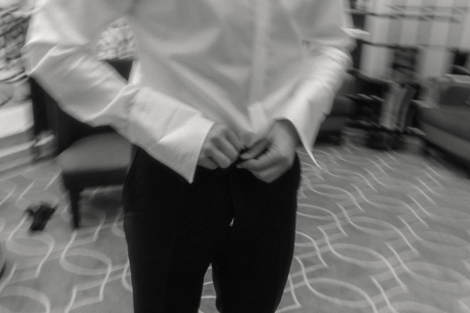 Black and white photo of a groom buttoning his dress shirt before a wedding ceremony.