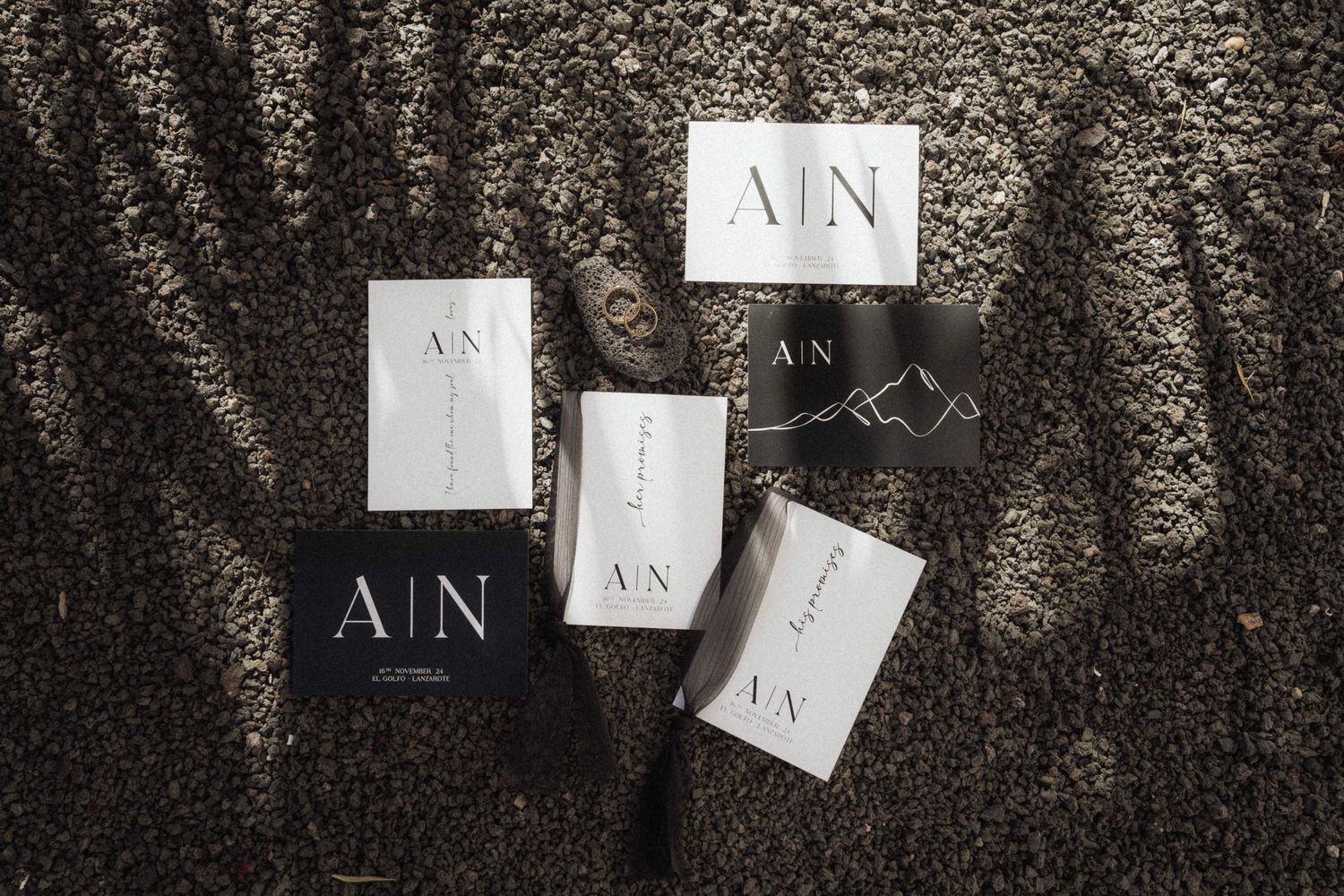 Black and white business cards with A|N logo scattered on textured surface with dramatic shadows.