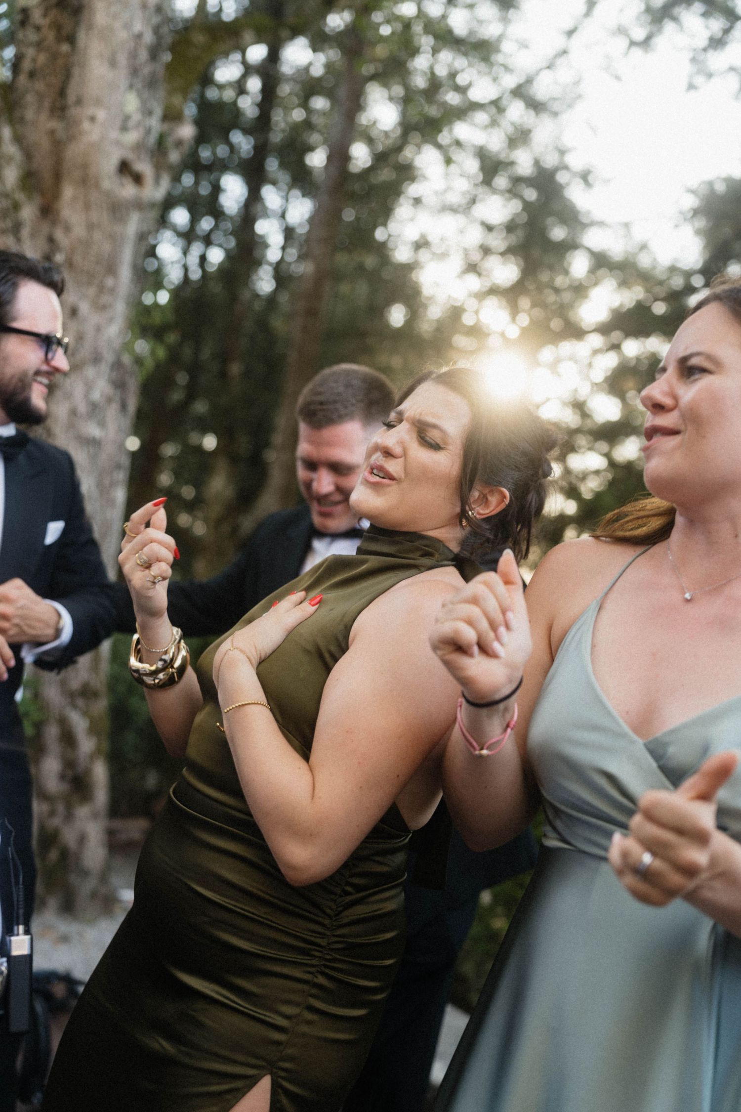 Wedding guests dancing joyfully in golden sunset light at outdoor reception with live entertainment.