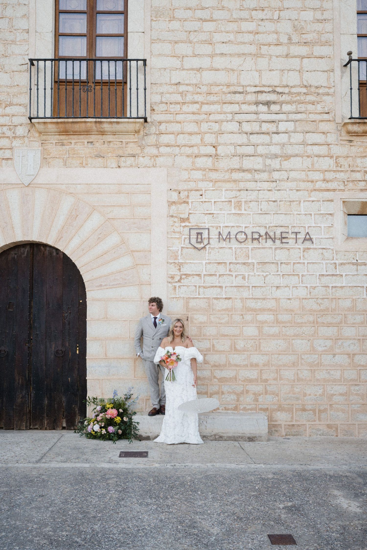 Bride and groom posing outside the historic Morneta building, bride holding a colorful bouquet in a white gown.