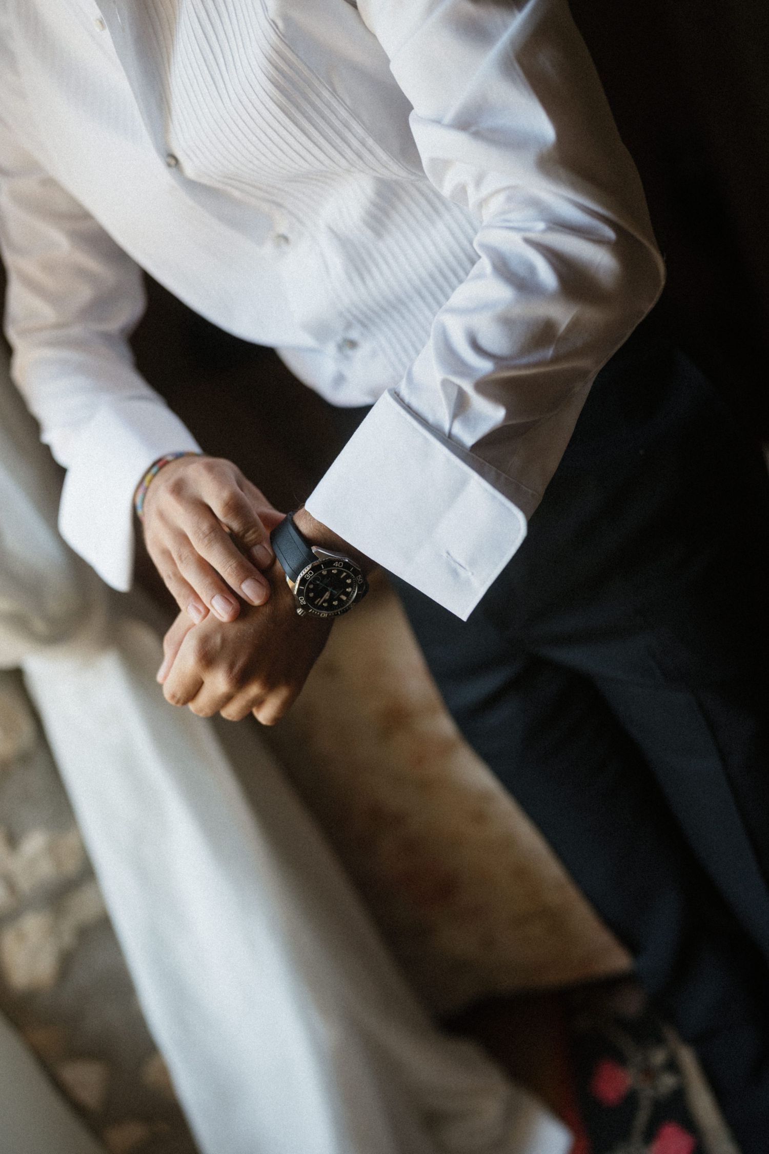 Groom adjusting his watch cufflinks wearing a white dress shirt and dark trousers on his wedding day.