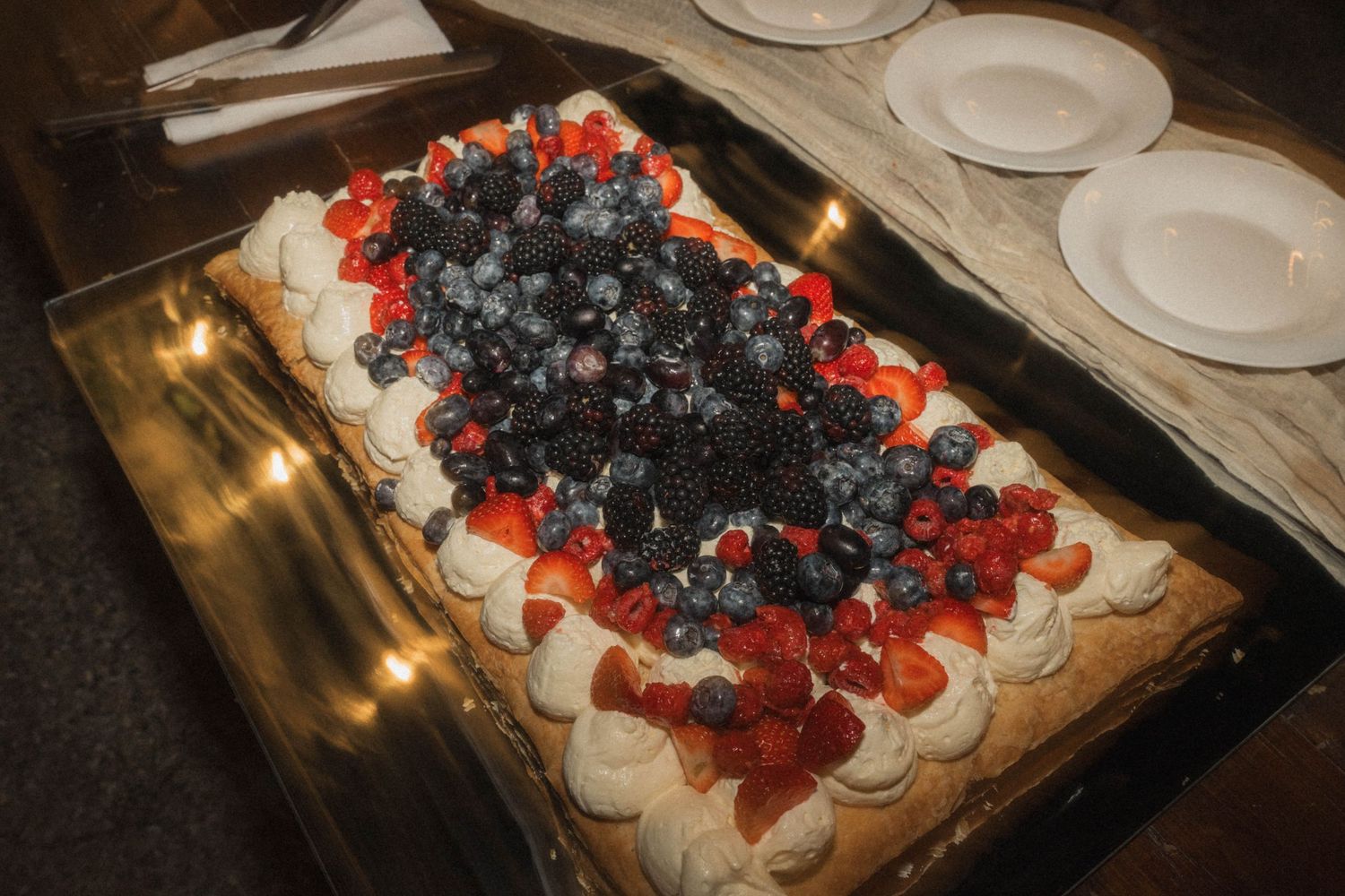 Rectangular wedding dessert cake topped with fresh strawberries and blueberries surrounded by candles at reception.