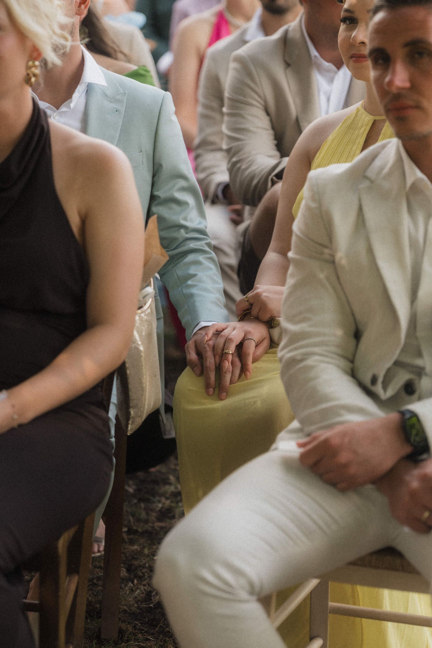 Wedding guests holding hands during an outdoor ceremony, man in white suit and woman in yellow dress.