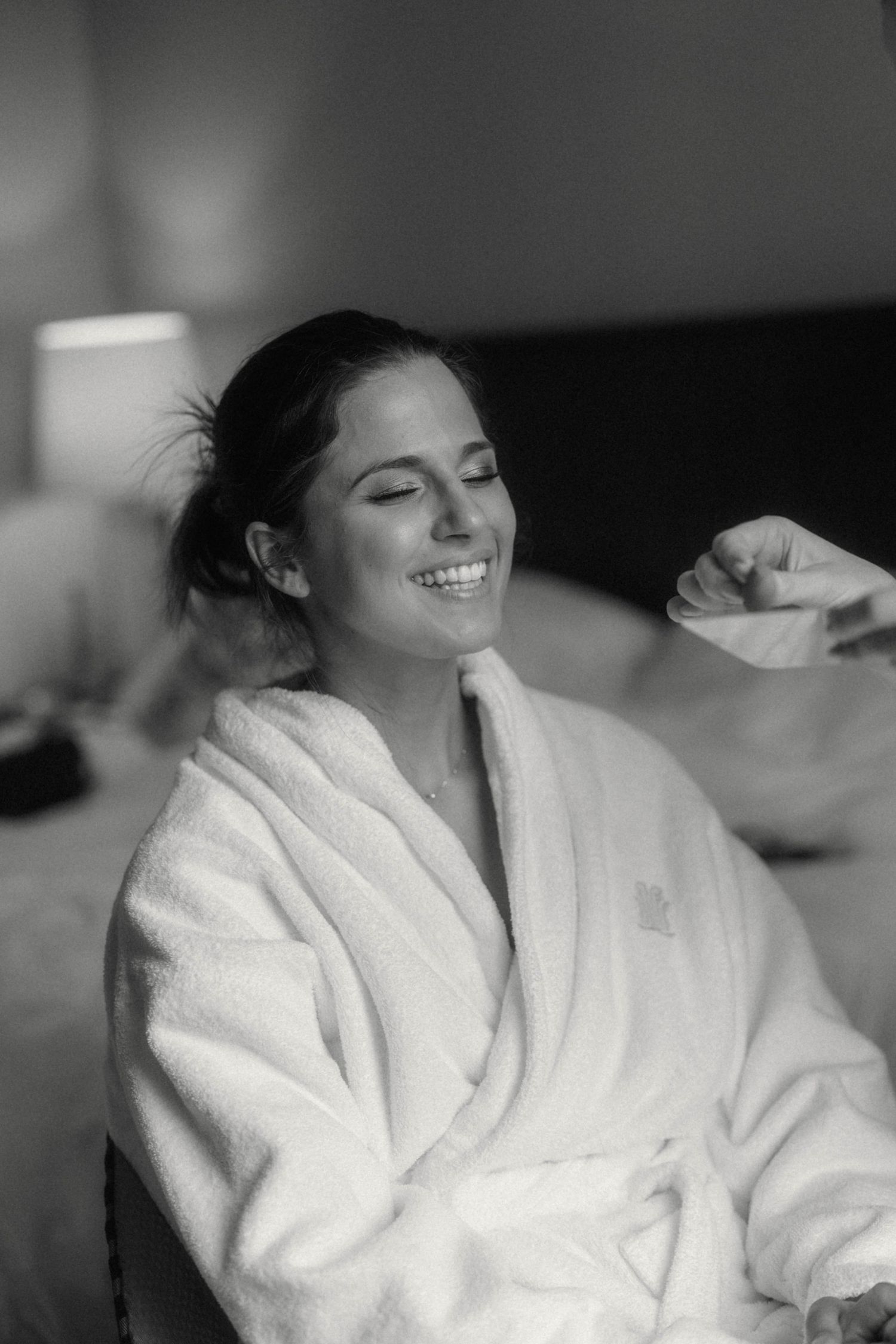 Smiling bride in white fluffy robe getting ready on her wedding day, black and white photo.