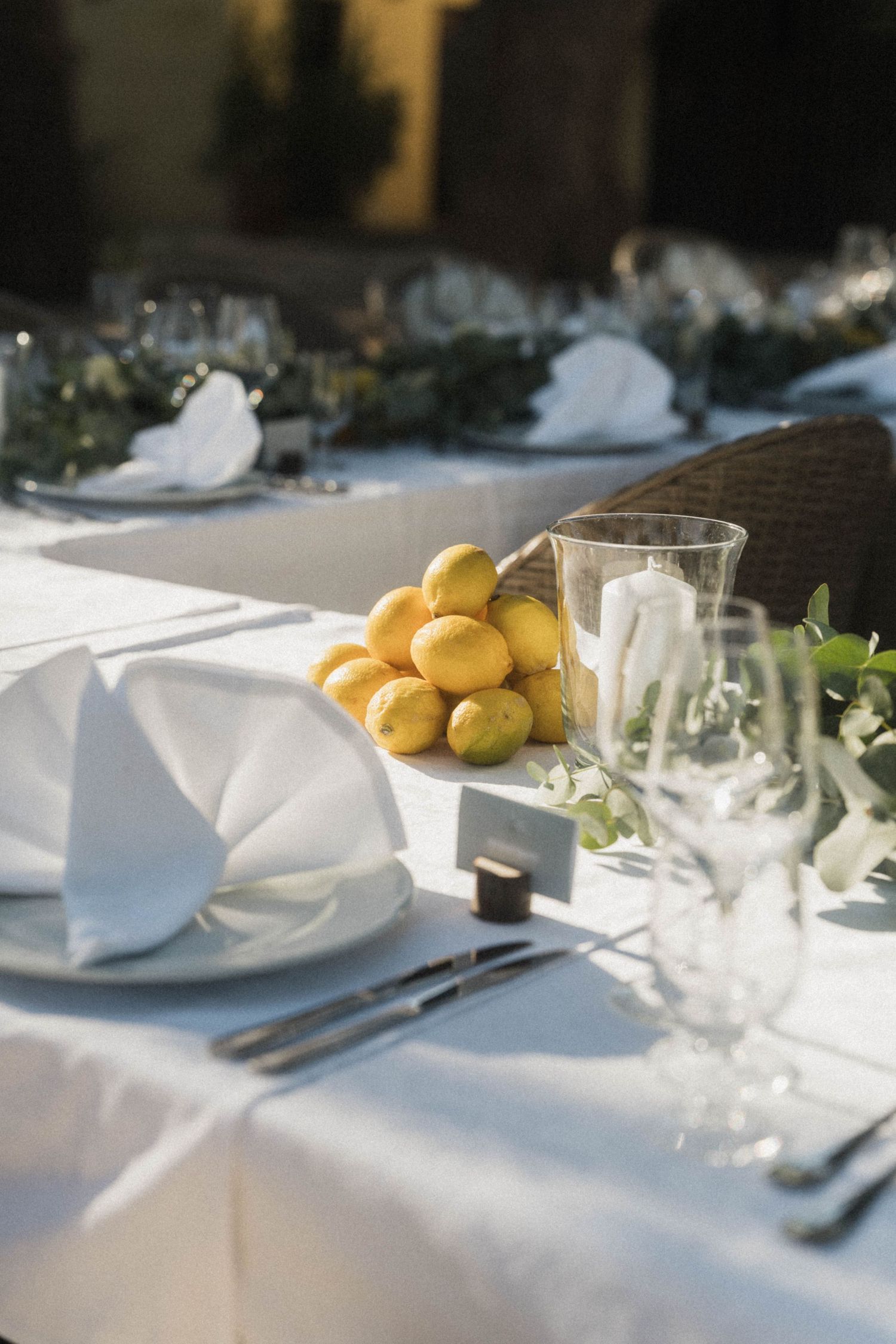 Elegant outdoor wedding table with fresh lemons centerpiece, white napkins, and crystal glassware.