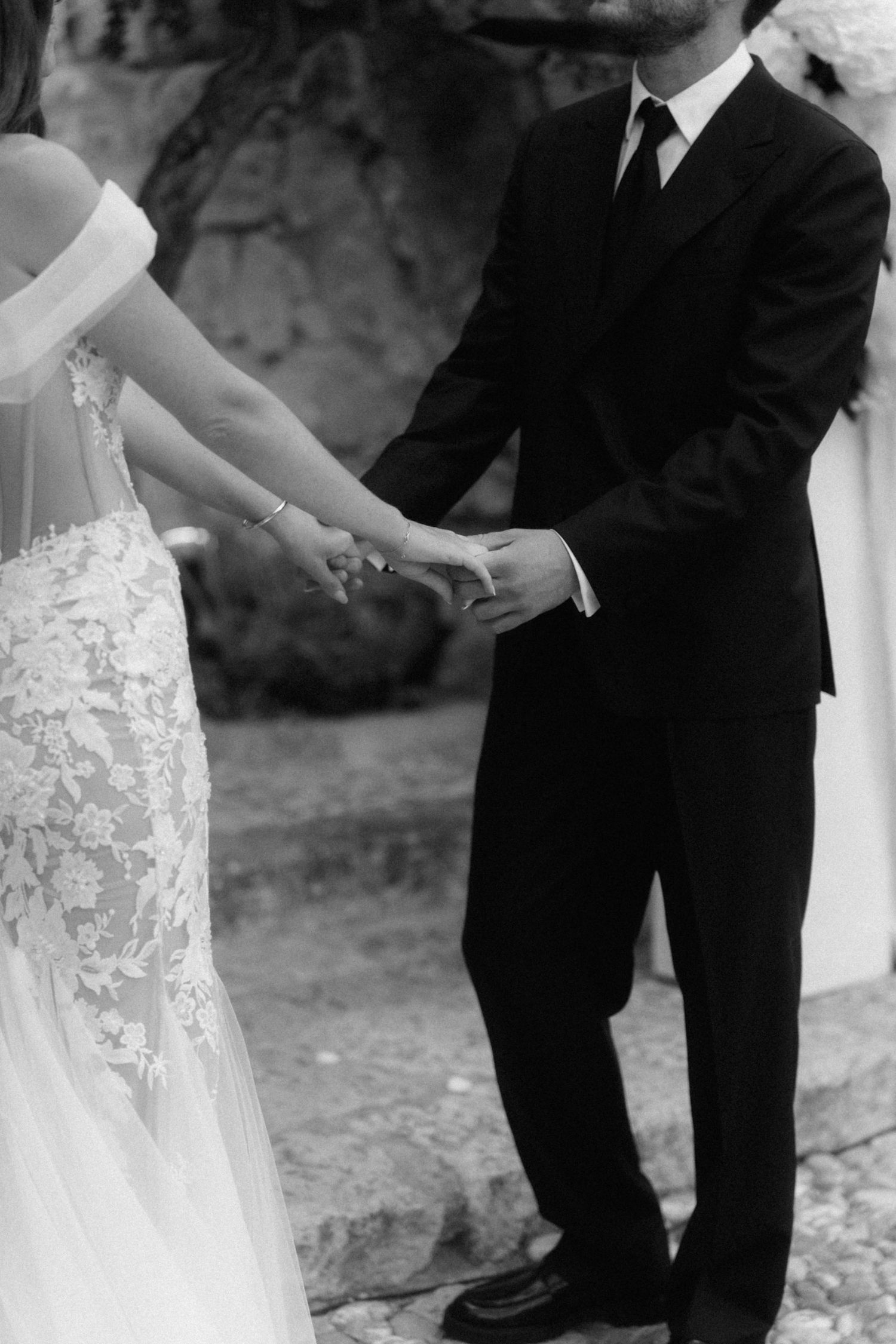 Black and white photo of bride and groom exchanging rings during outdoor wedding ceremony.