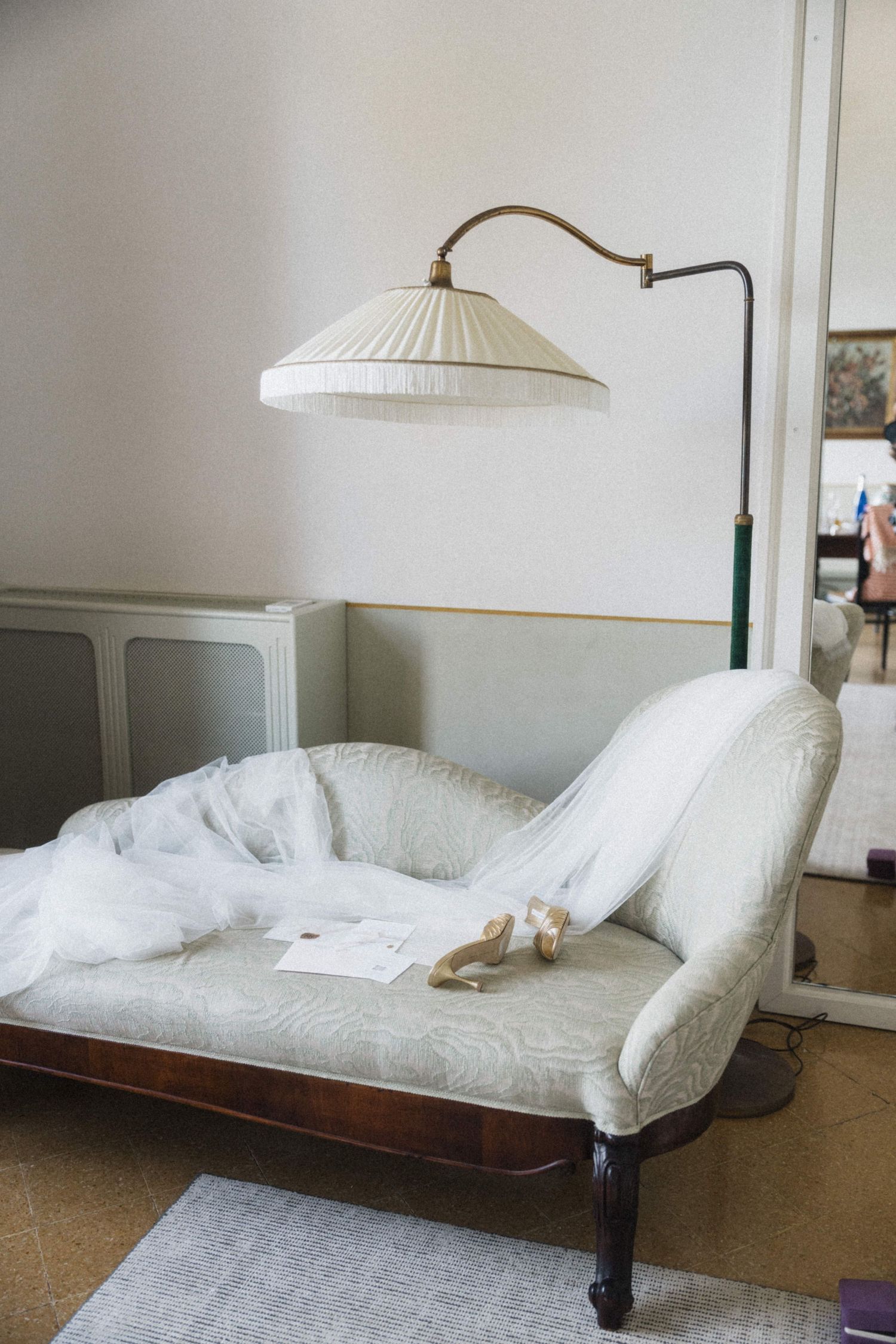 Bridal veil and gold heels draped over vintage chaise lounge beneath an elegant arc floor lamp.