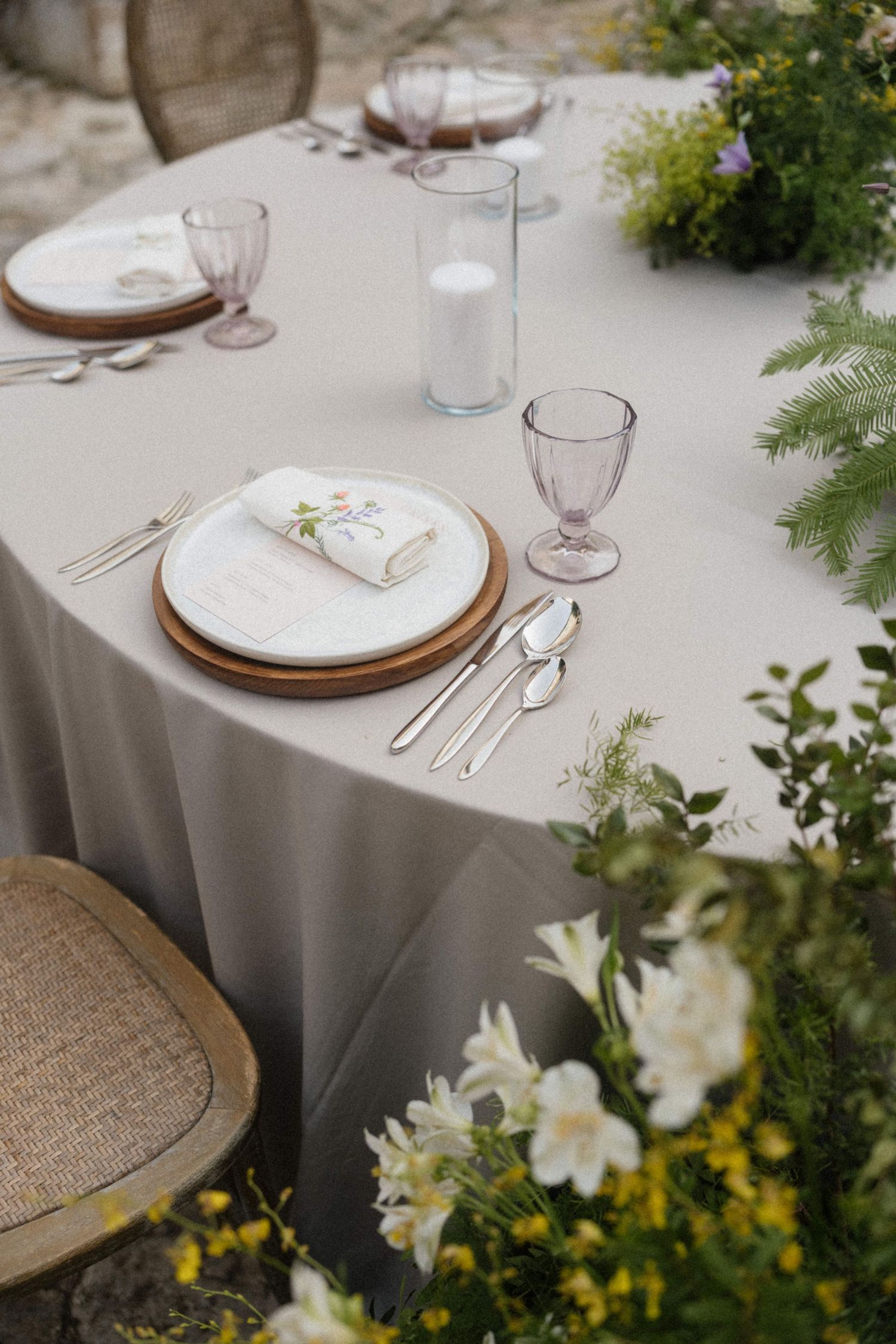 Elegant outdoor wedding reception table set with linen, wooden chargers, pink glassware, and fresh flowers.