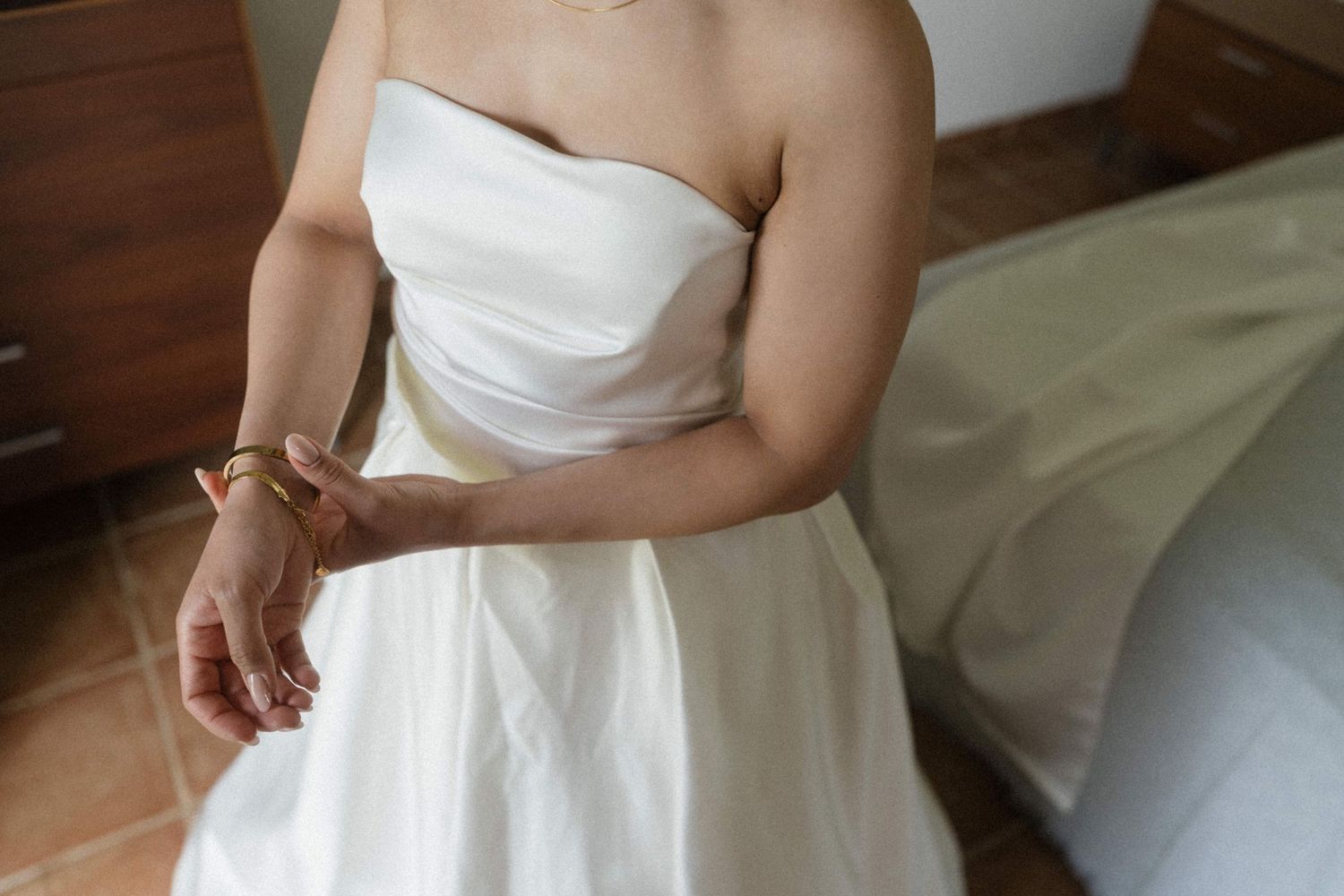 Bride in a strapless white wedding gown adjusting her bracelet while getting ready indoors.