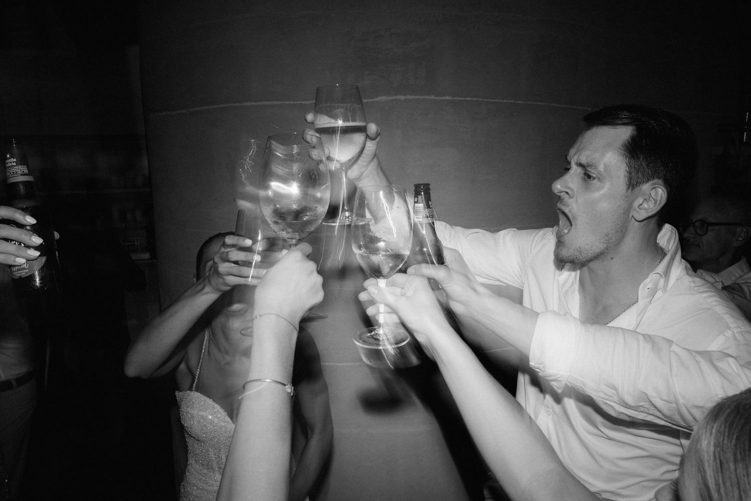 Black and white photo of wedding guests clinking wine glasses together in a lively toast on the dance floor.
