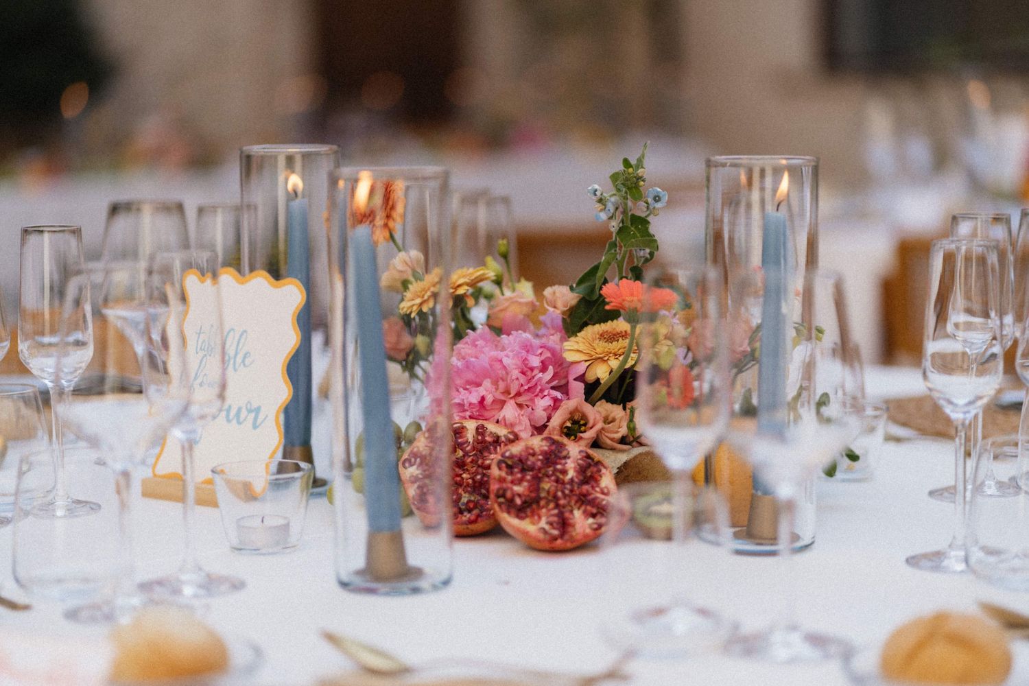 Elegant wedding table centerpiece with blue taper candles, pink peonies, pomegranate, and crystal glassware.