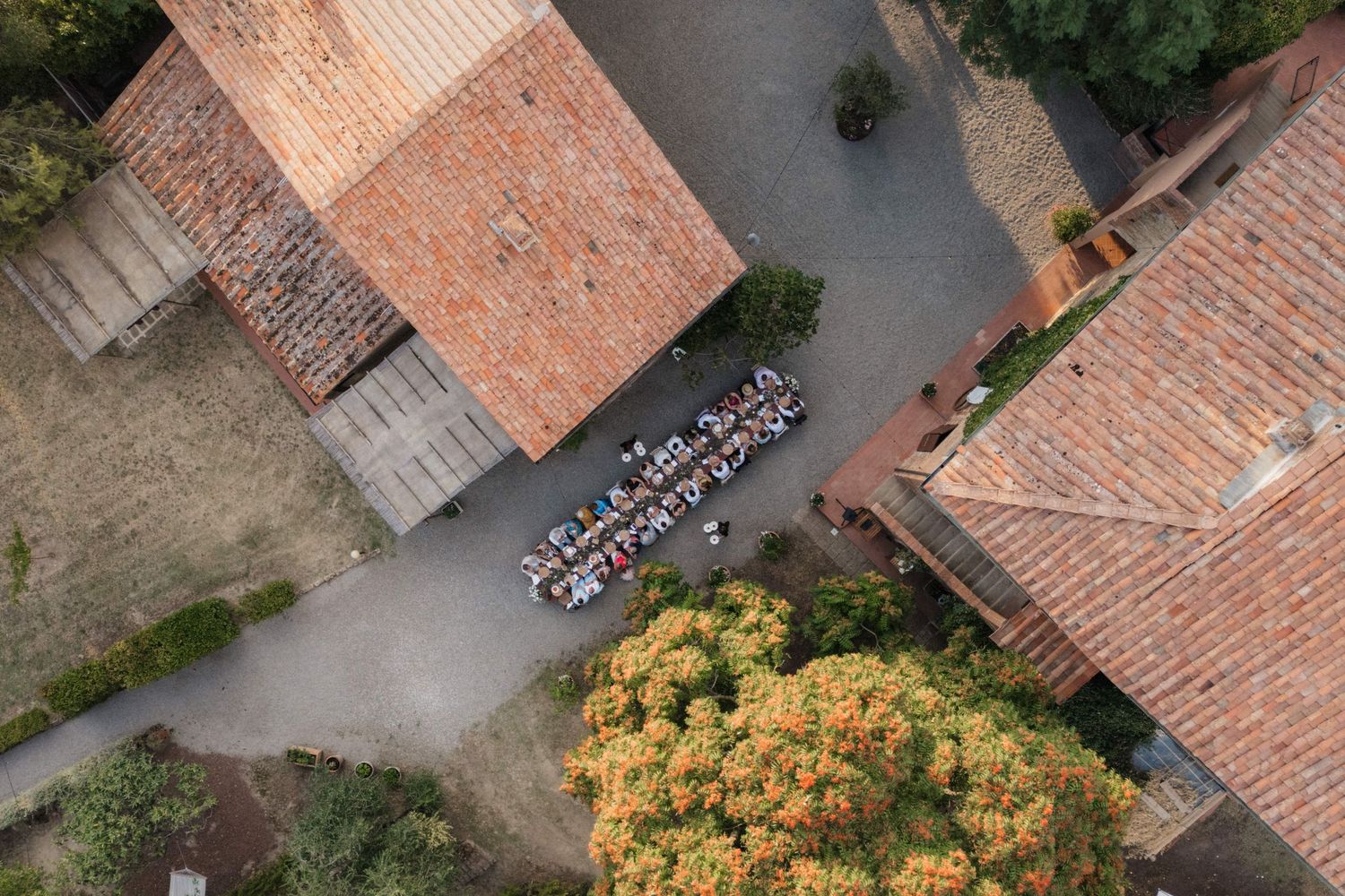 Aerial view of wedding guests seated between rustic stone buildings at a Tuscan countryside estate.