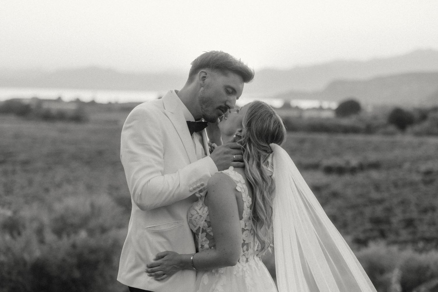 Black and white romantic portrait of bride and groom embracing in vineyard landscape.