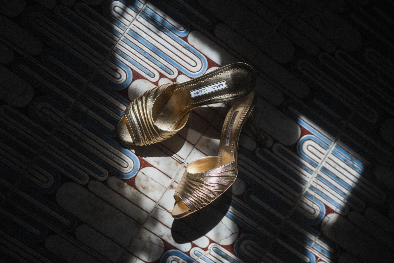 Gold strappy bridal heels casting shadows on decorative patterned tile floor in natural light.
