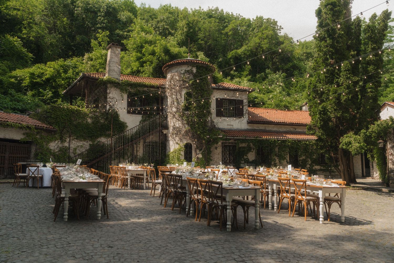 Rustic stone venue with long banquet tables set for an outdoor wedding reception surrounded by lush greenery.