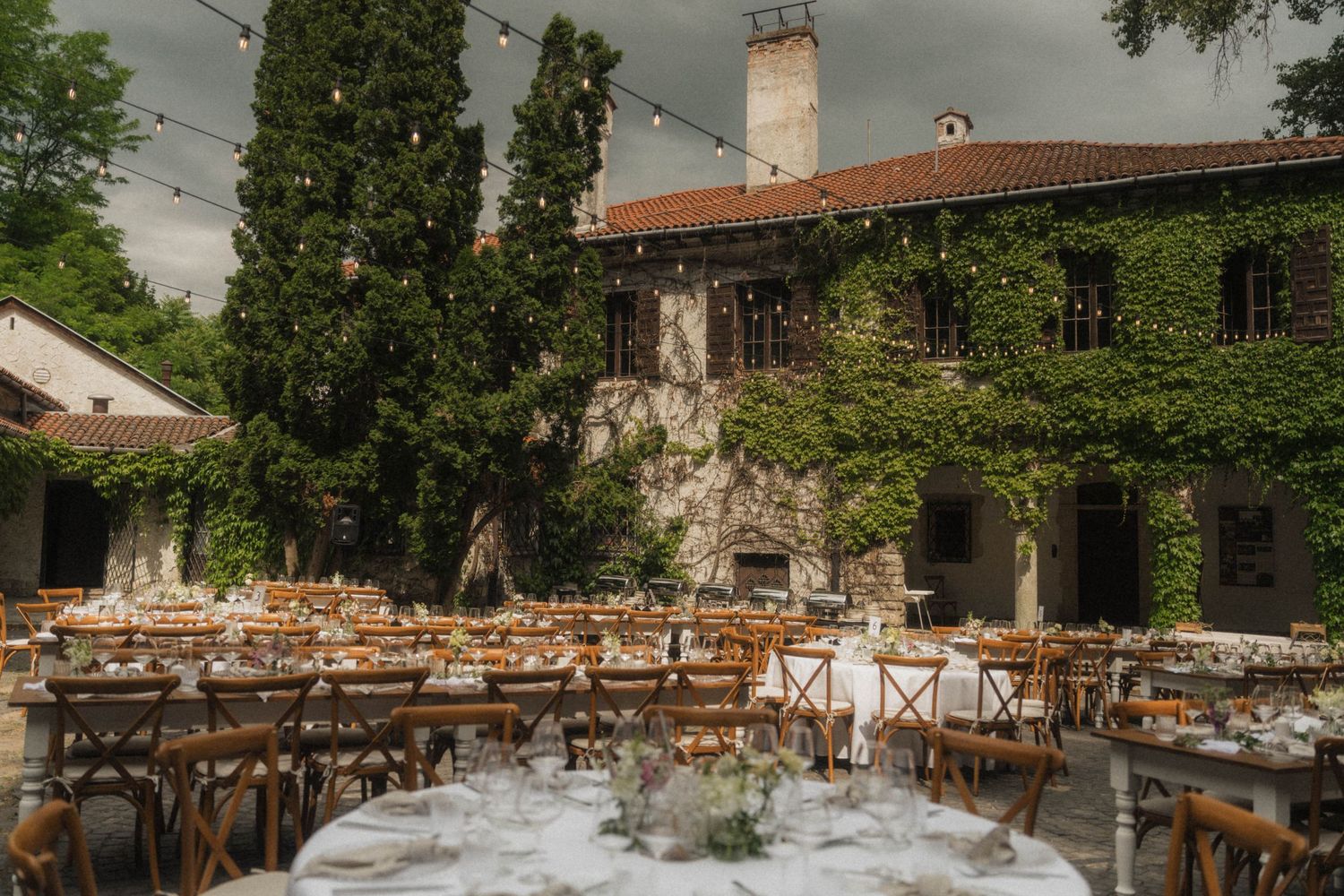 Elegant outdoor wedding reception in ivy-covered stone villa courtyard with string lights and long dining tables.
