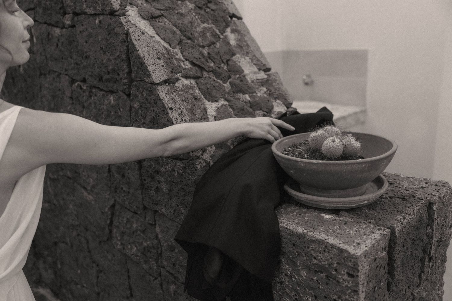 Woman placing fruit bowl on rustic stone ledge in black and white artistic photography.