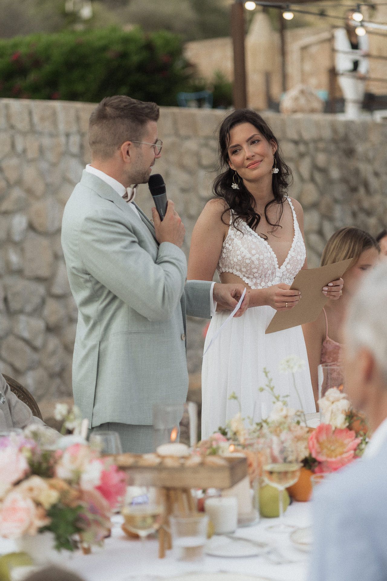 Bride and groom sharing vows outdoors at elegant wedding reception with floral table arrangements.