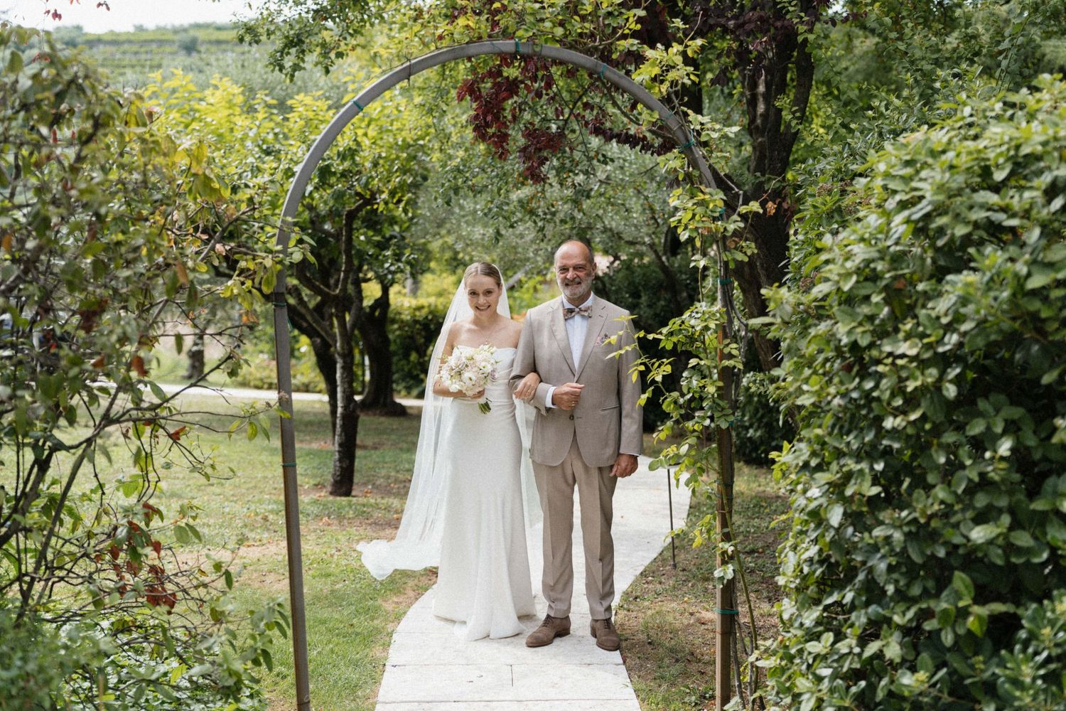 Bride and groom standing under a floral arch in a lush garden during an outdoor wedding ceremony.