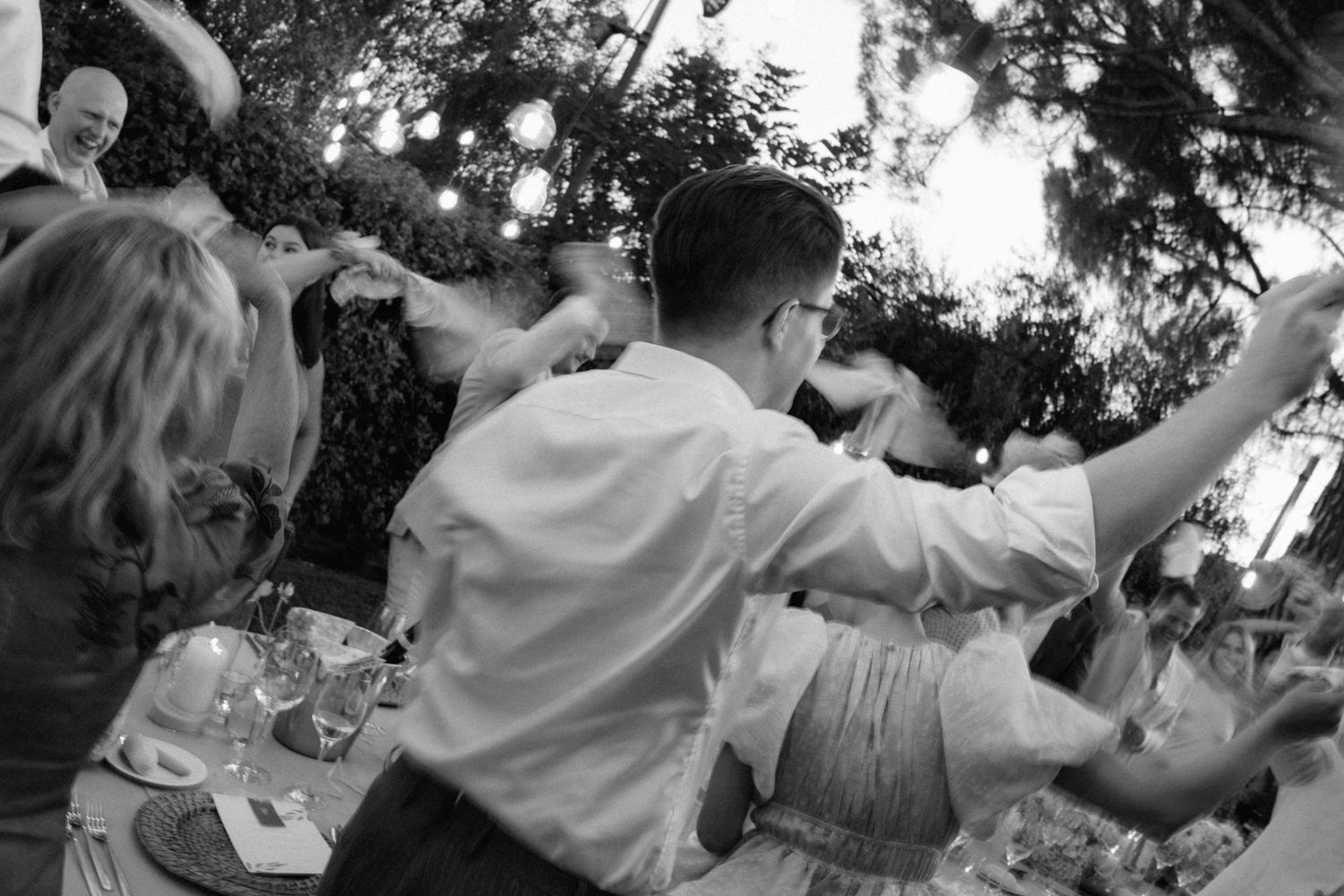 Black and white photo of guests dancing outdoors at an elegant evening wedding reception under string lights.