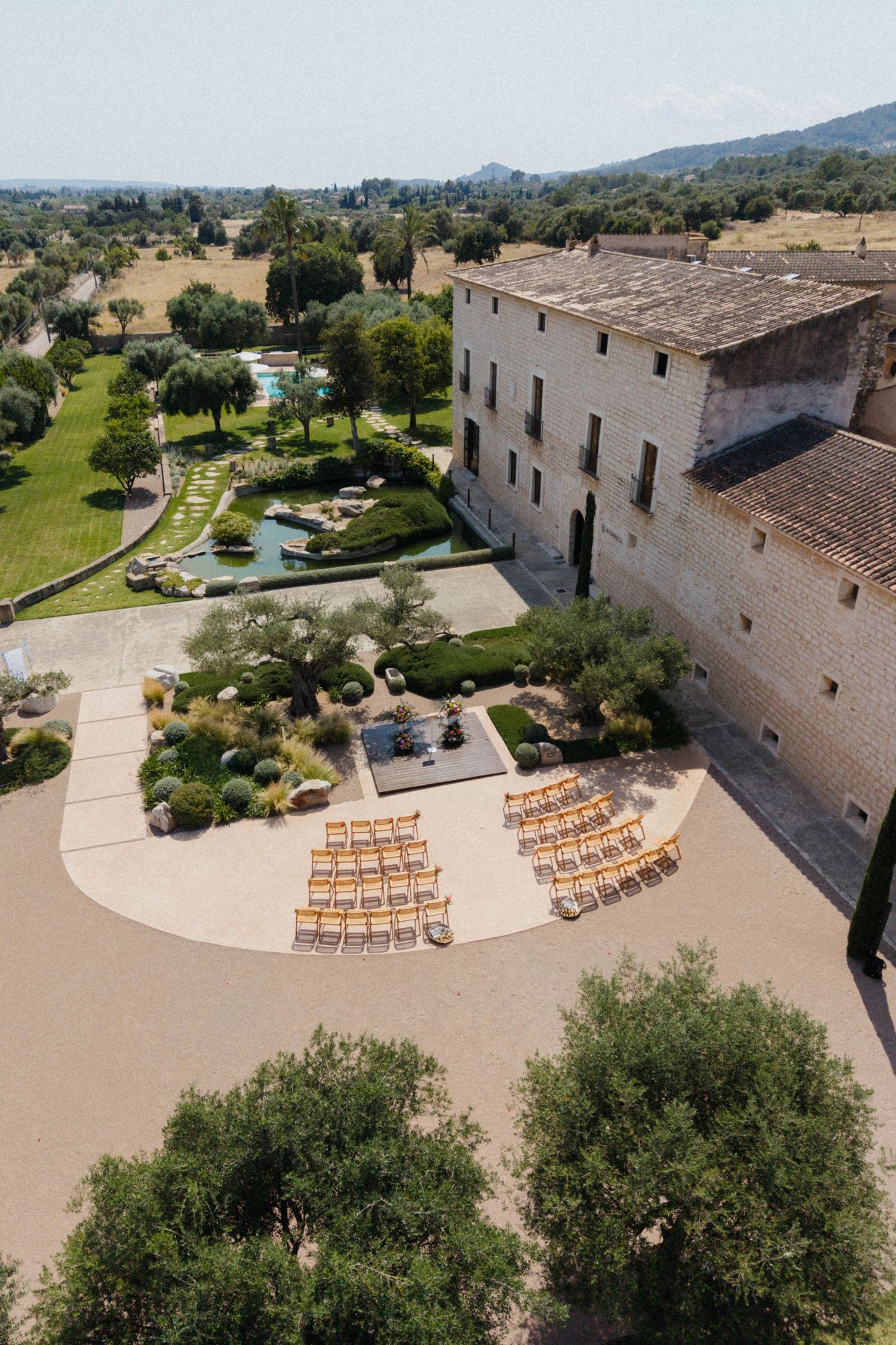 Aerial view of a rustic stone wedding venue with outdoor ceremony chairs and lush gardens.