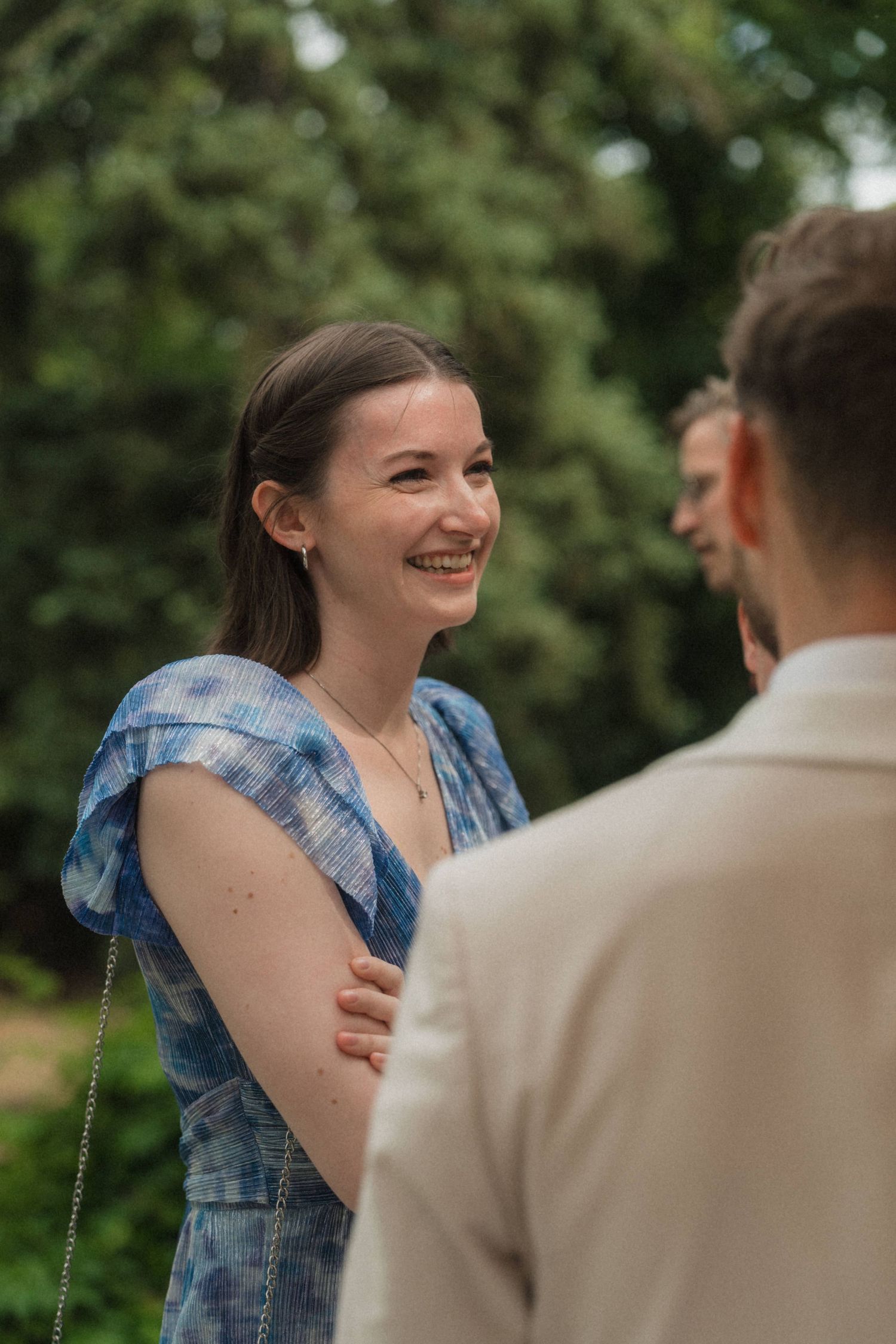 Smiling woman in a blue dress laughing with a man in a beige suit at an outdoor wedding event.