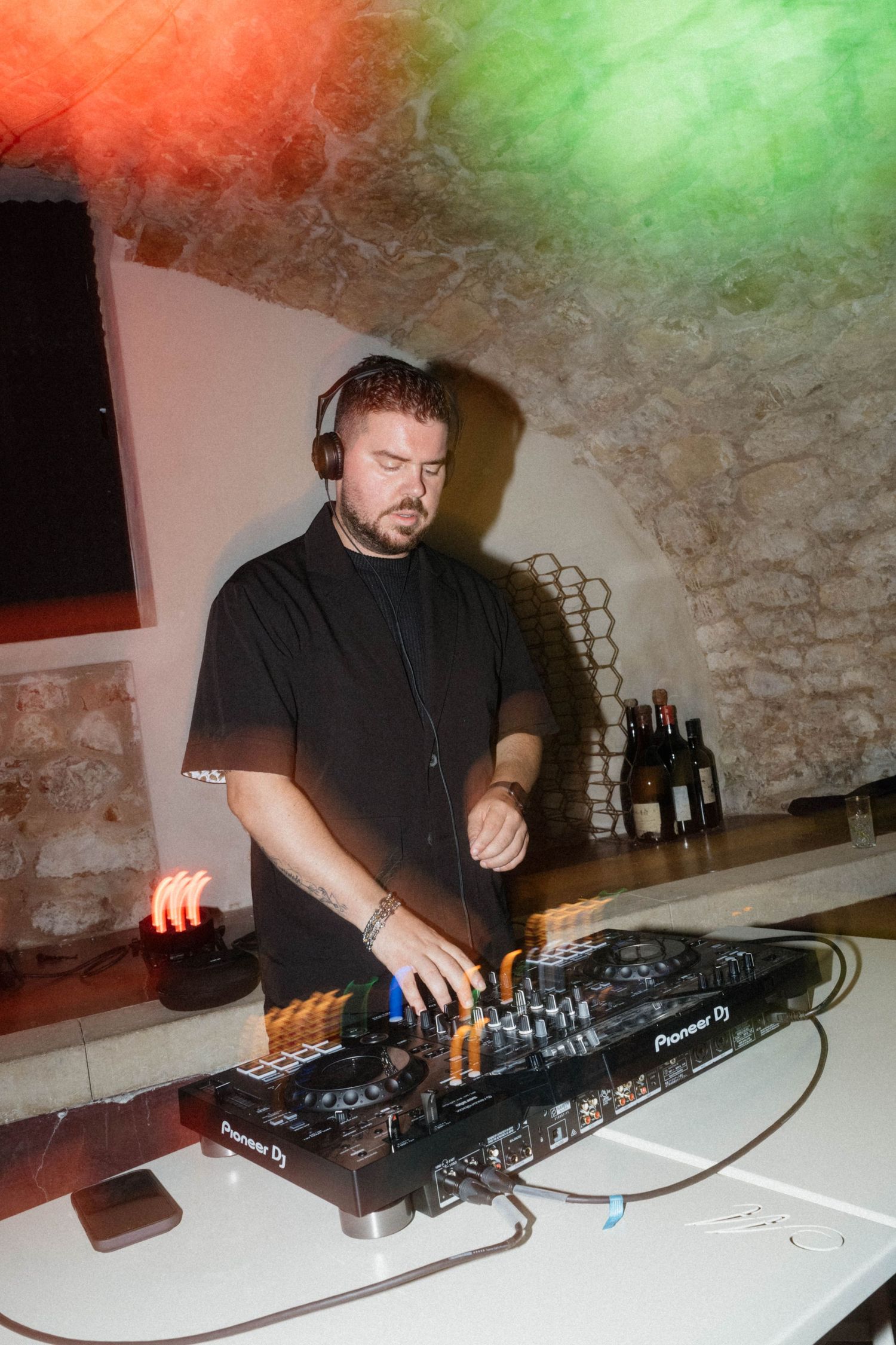 DJ mixing on Pioneer DJ controller in stone venue with red and green stage lighting.