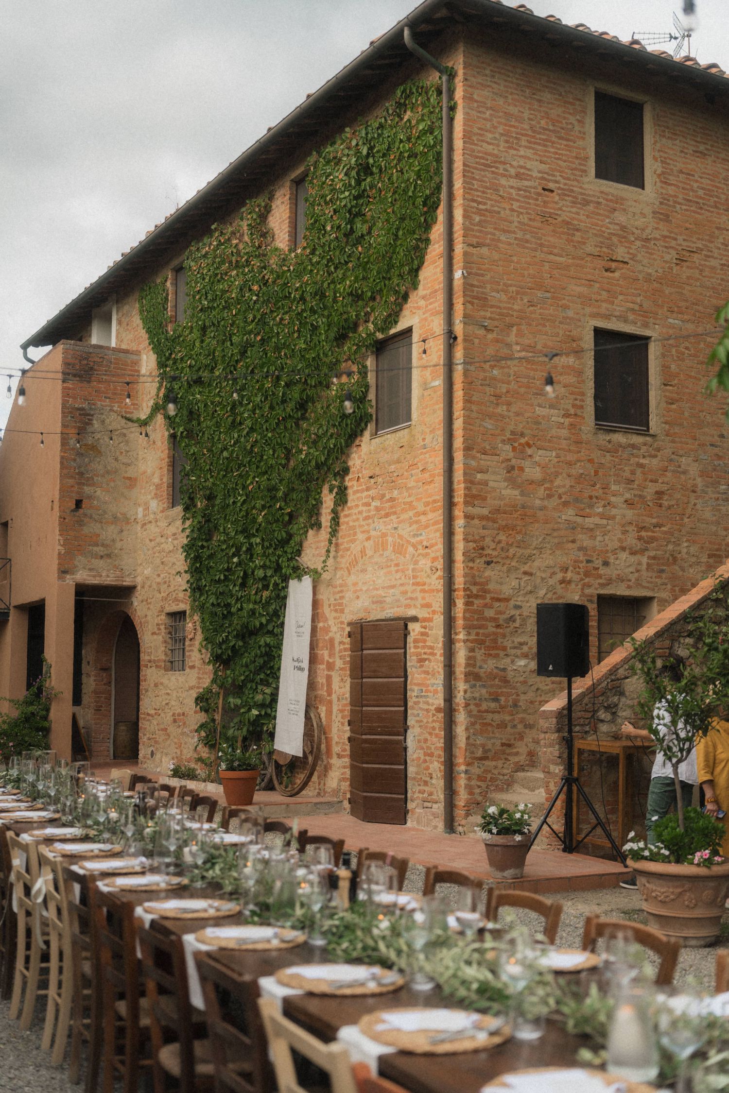 Elegant outdoor wedding reception set along a rustic Tuscan brick villa with ivy-covered walls and long decorated tables.