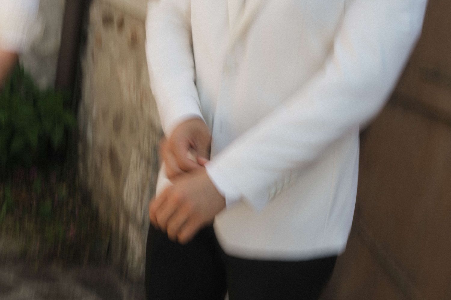 Person in white jacket standing with hands clasped behind their back outdoors.