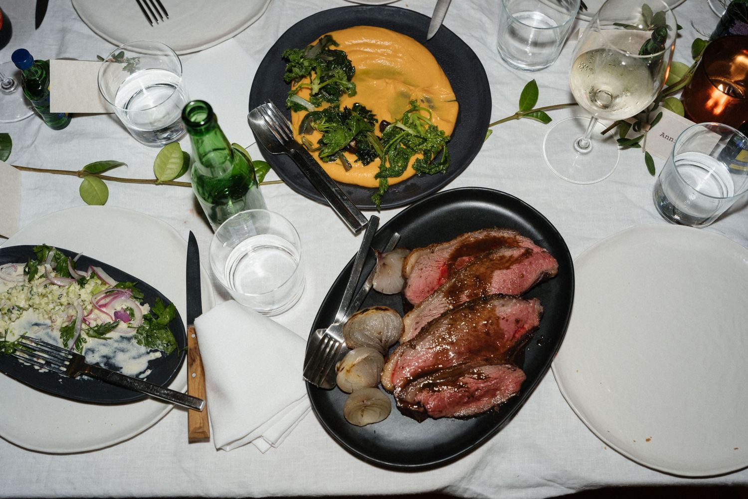 A wedding dinner table with plates of sliced roast beef with potatoes, a creamy dish with greens, salad, and wine glasses.