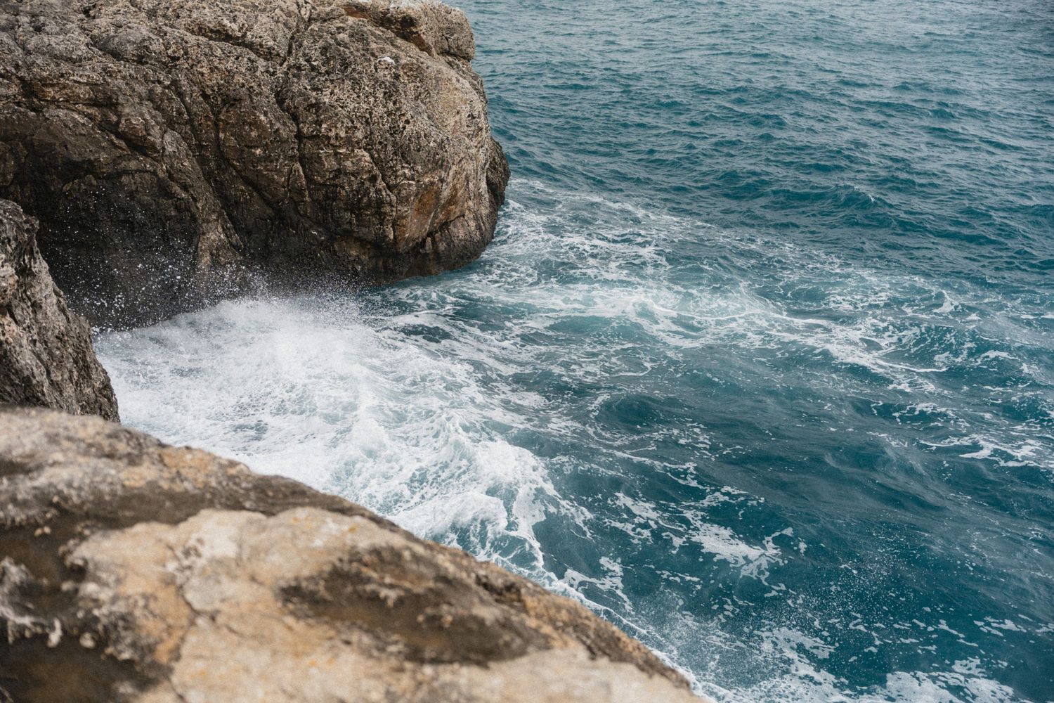 Rocky coastal cliffs with turquoise ocean waves crashing against the shore, creating white sea foam.