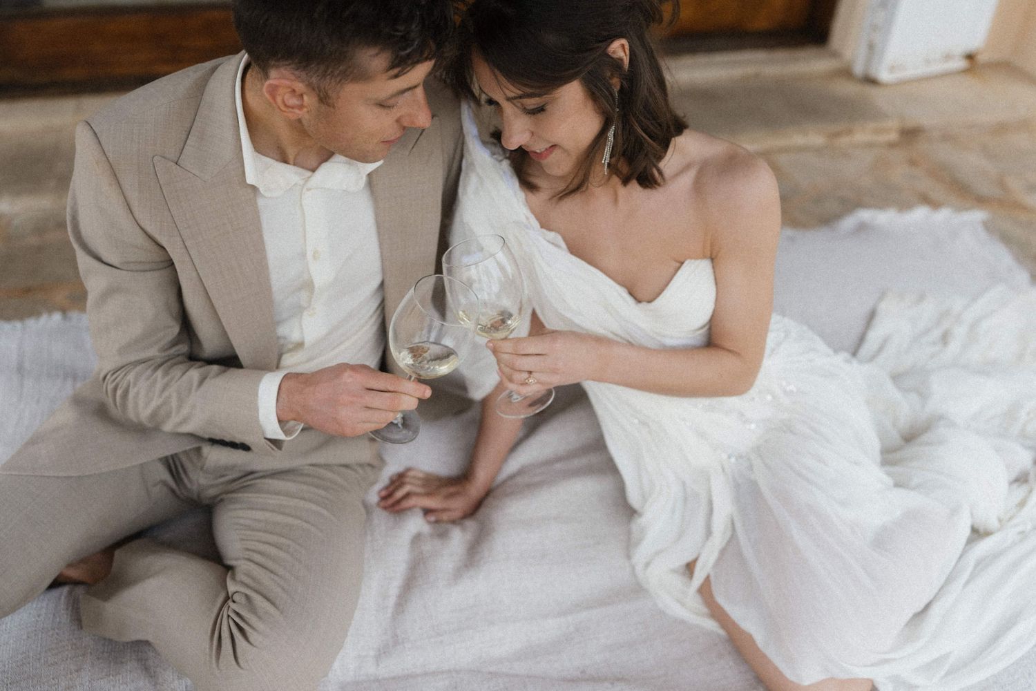 Bride and groom in elegant attire toasting with wine glasses while sitting together.