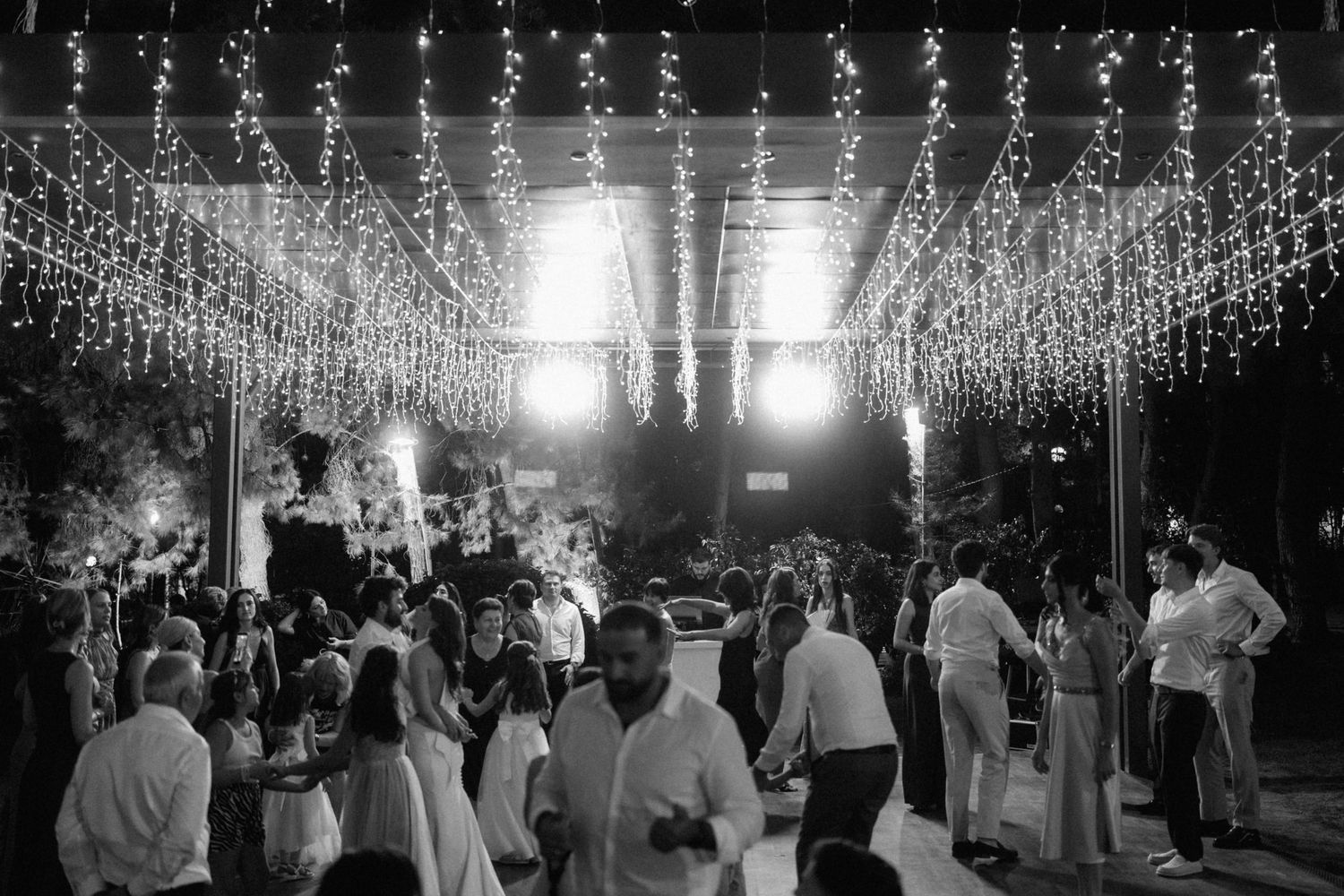 Black and white photo of elegant outdoor wedding reception with string lights canopy and guests dancing at night.