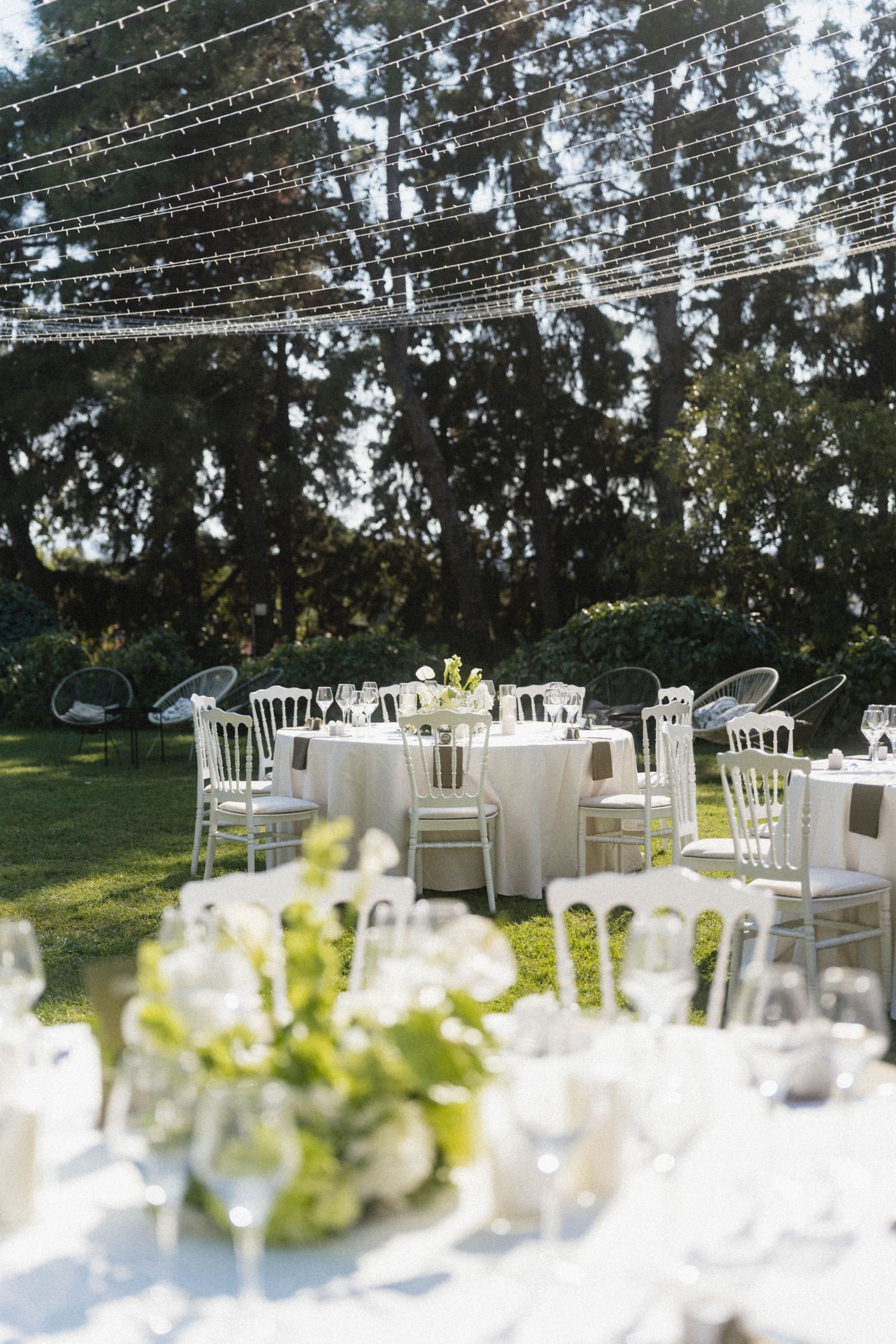 Romantic outdoor wedding reception with white chiavari chairs, round tables, and string lights draped above a lush garden.