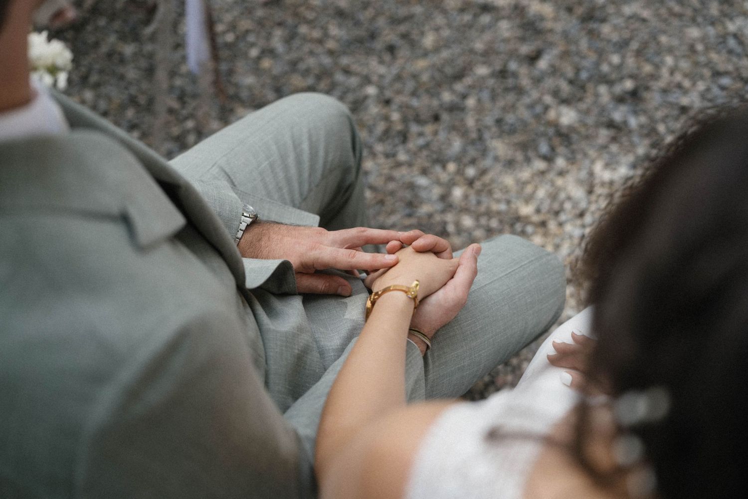 Close-up of bride and groom holding hands, bride wearing gold bracelet, groom in grey suit.