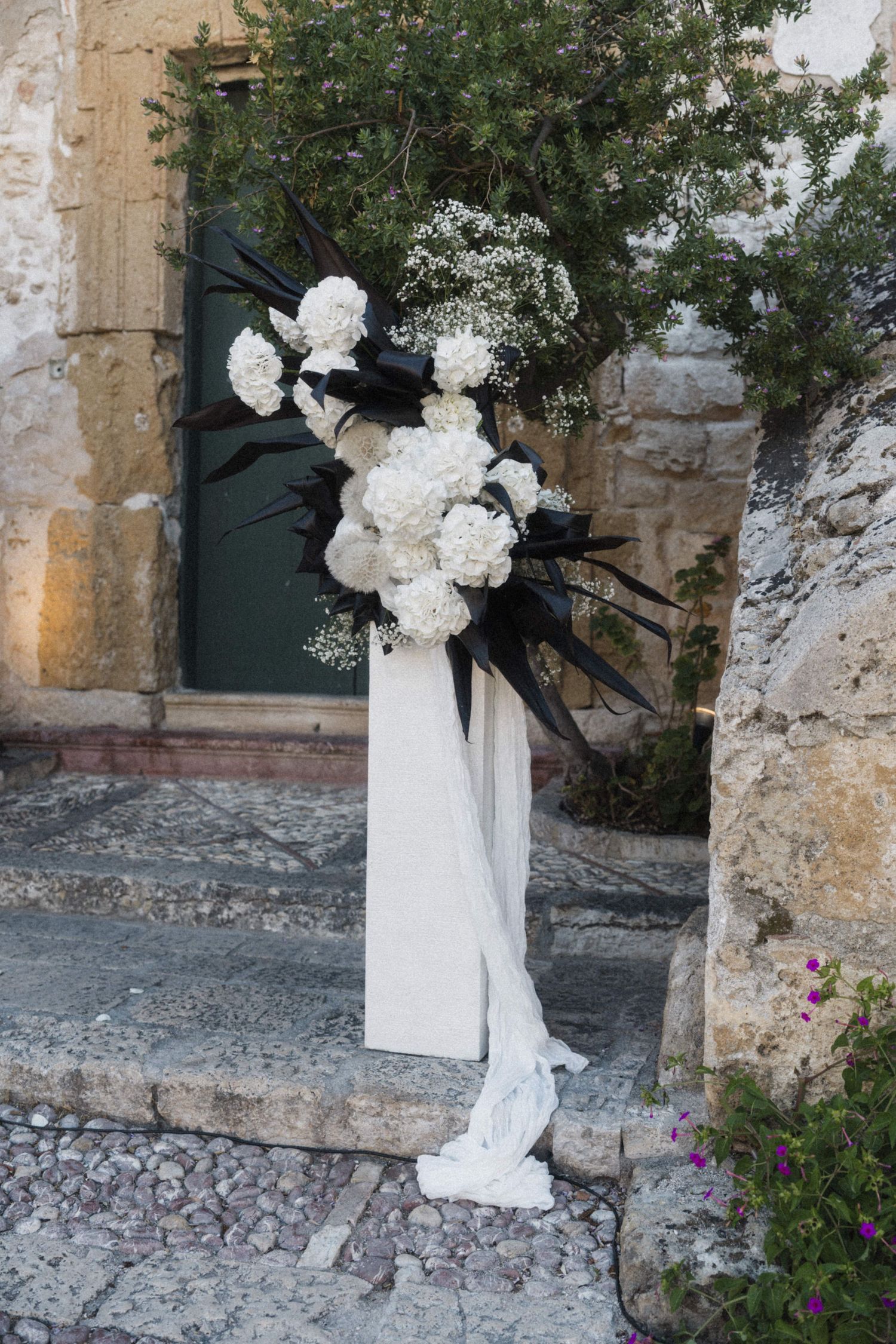Elegant wedding floral arrangement with white hydrangeas and black feathers on stone steps.