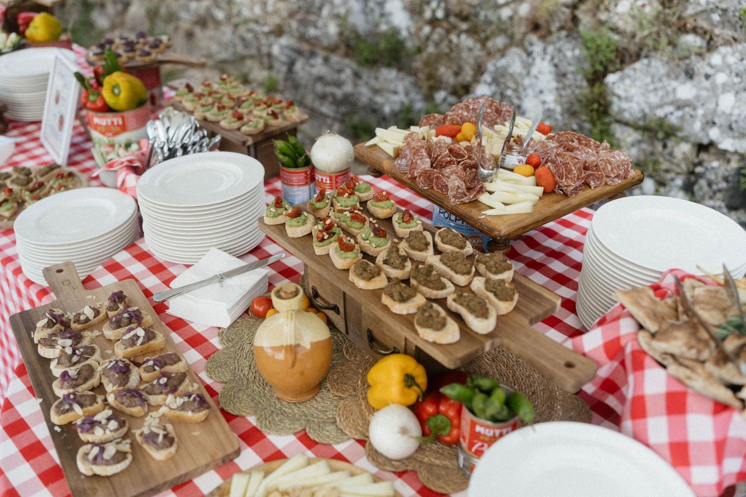 Rustic Italian-themed wedding food display with charcuterie, appetizers, and red checkered tablecloth decoration.