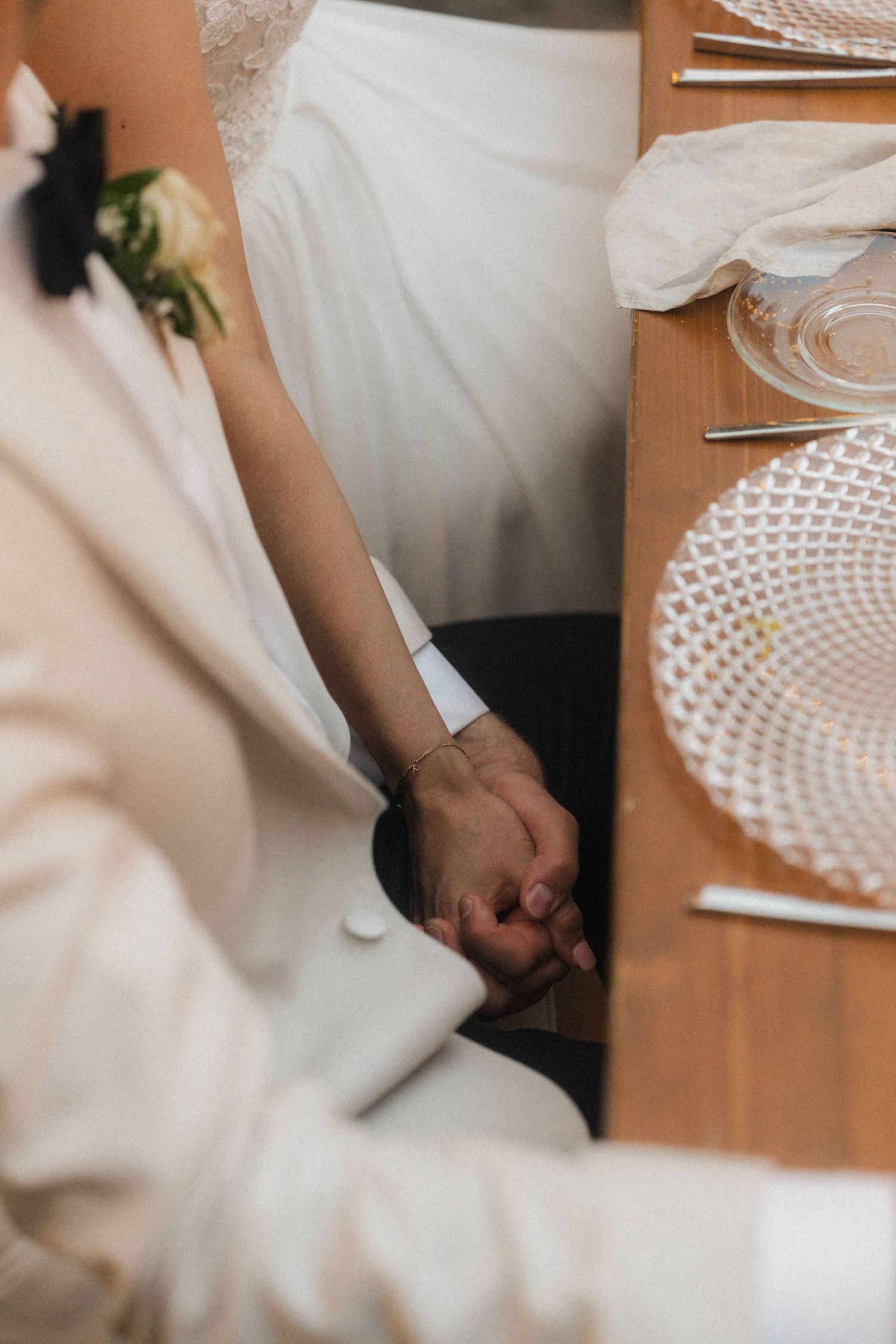 Bride and groom holding hands under the table during their wedding reception dinner.
