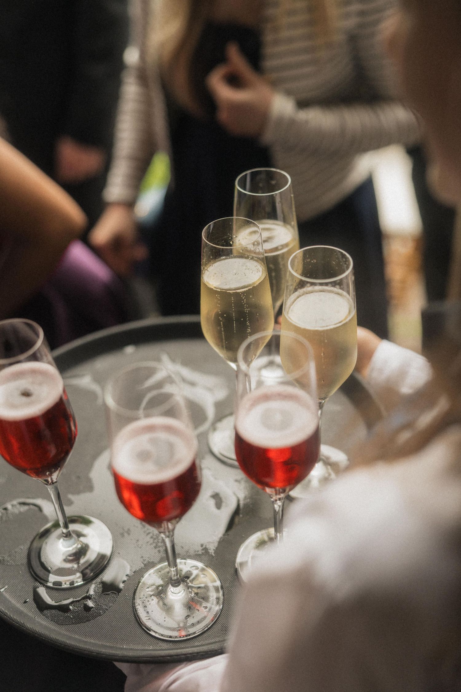 Server holding tray of champagne and red wine glasses at wedding reception.