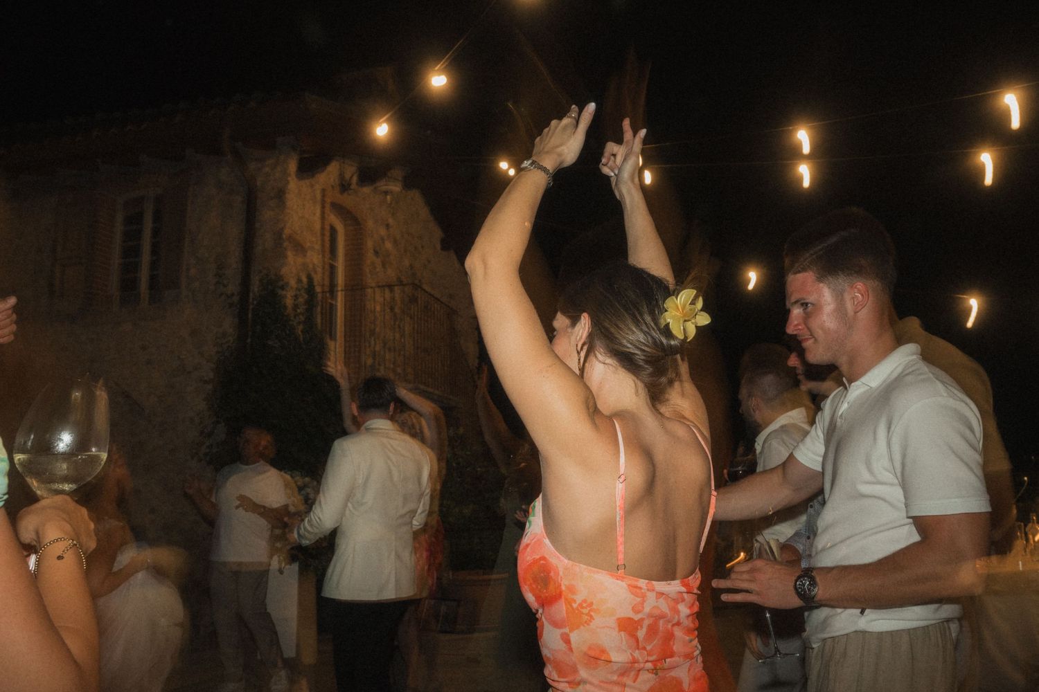 Guests dancing outdoors at night under warm string lights at wedding reception.