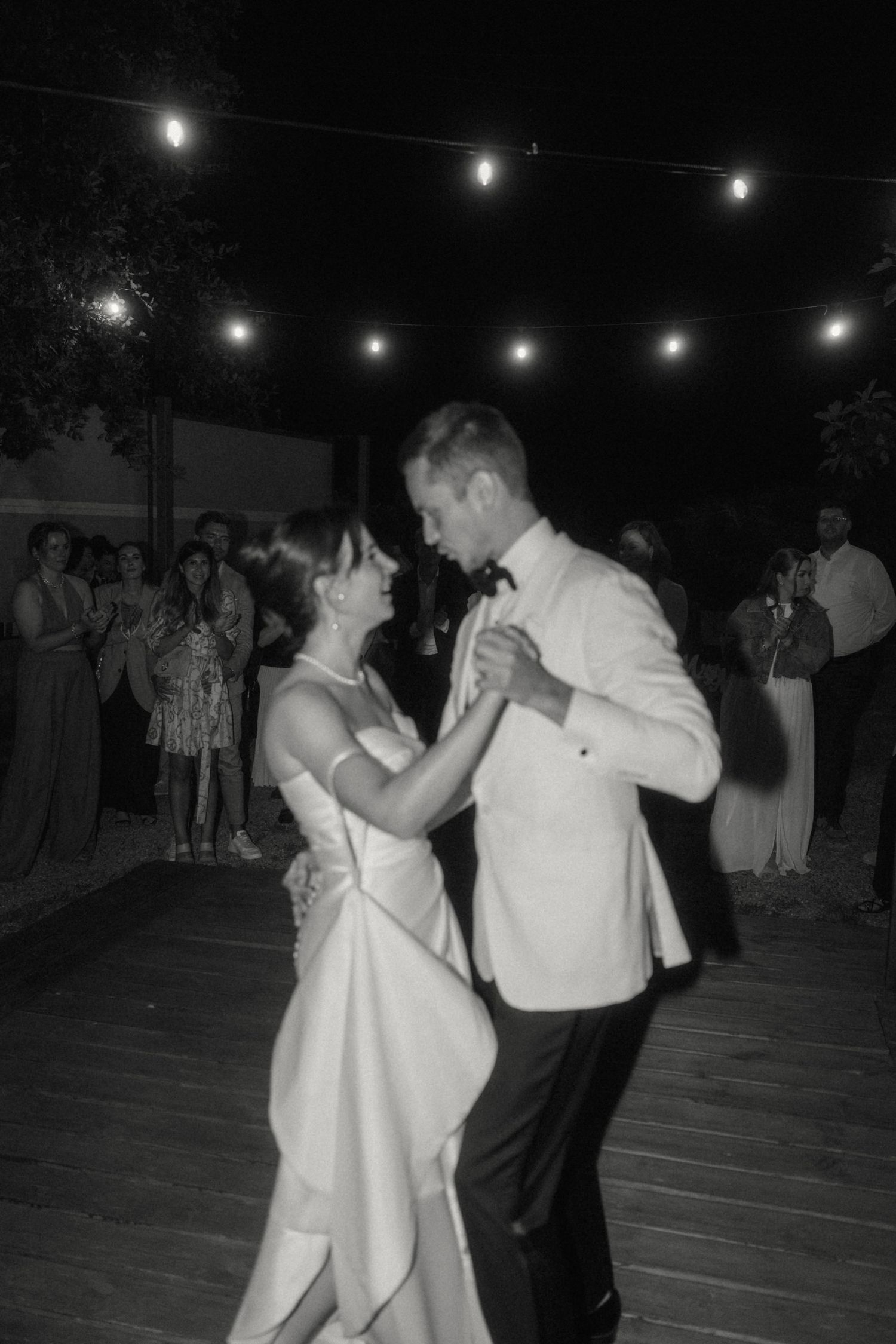 Bride and groom sharing their first dance under string lights at an outdoor evening wedding reception.