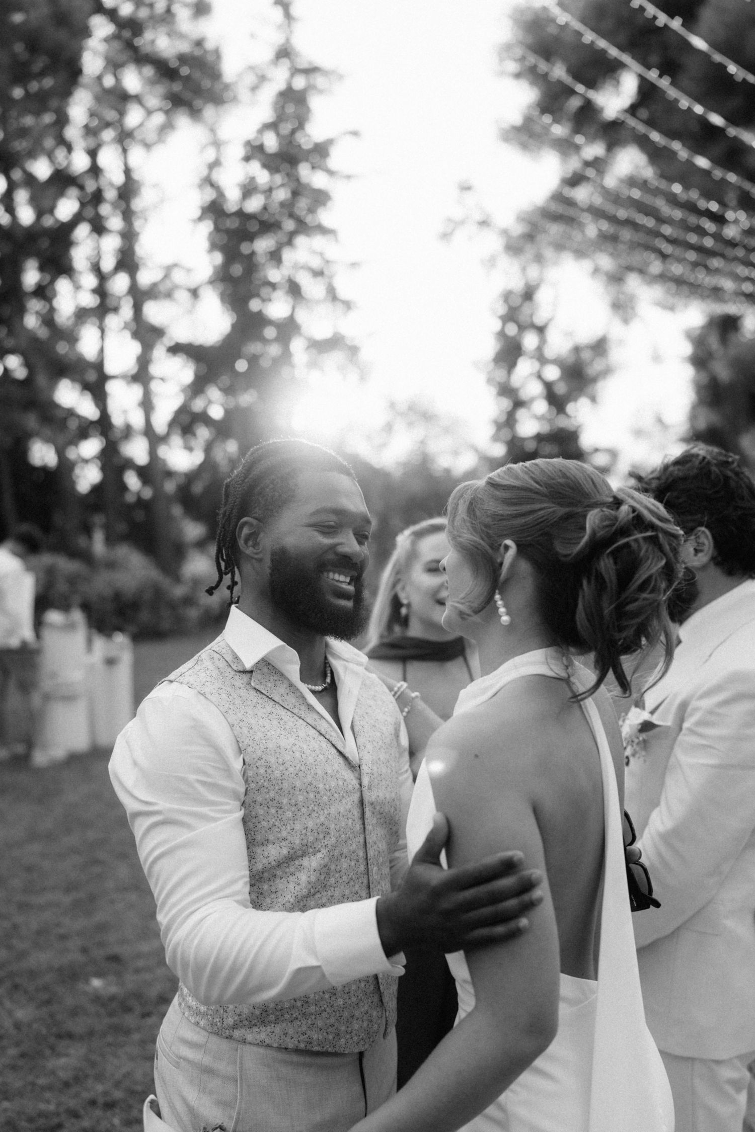 Black and white photo of a smiling groom dancing with his bride at an outdoor wedding reception.